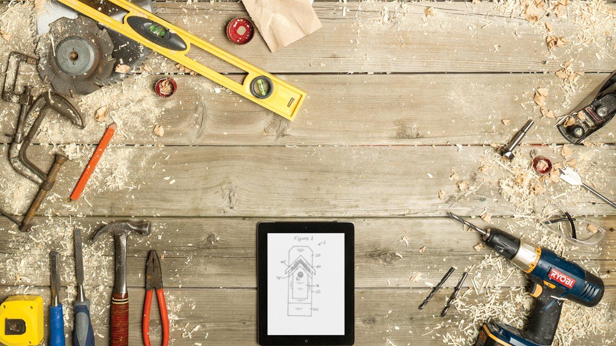 Tools and sawdust on wood surround an e-reader displaying a blueprint.