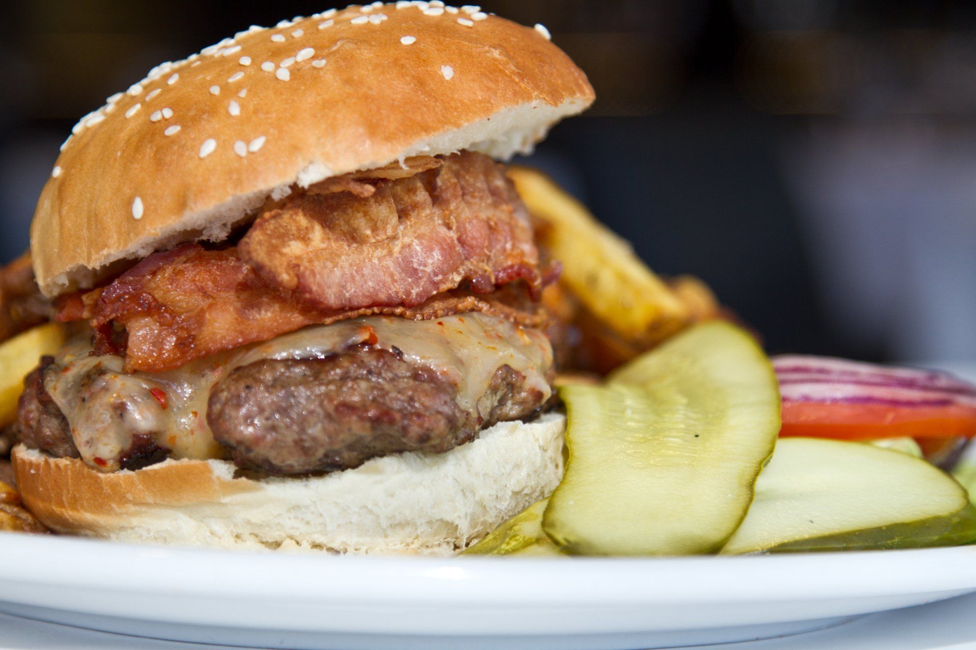 Bacon cheeseburger with fries and pickles on a white plate.