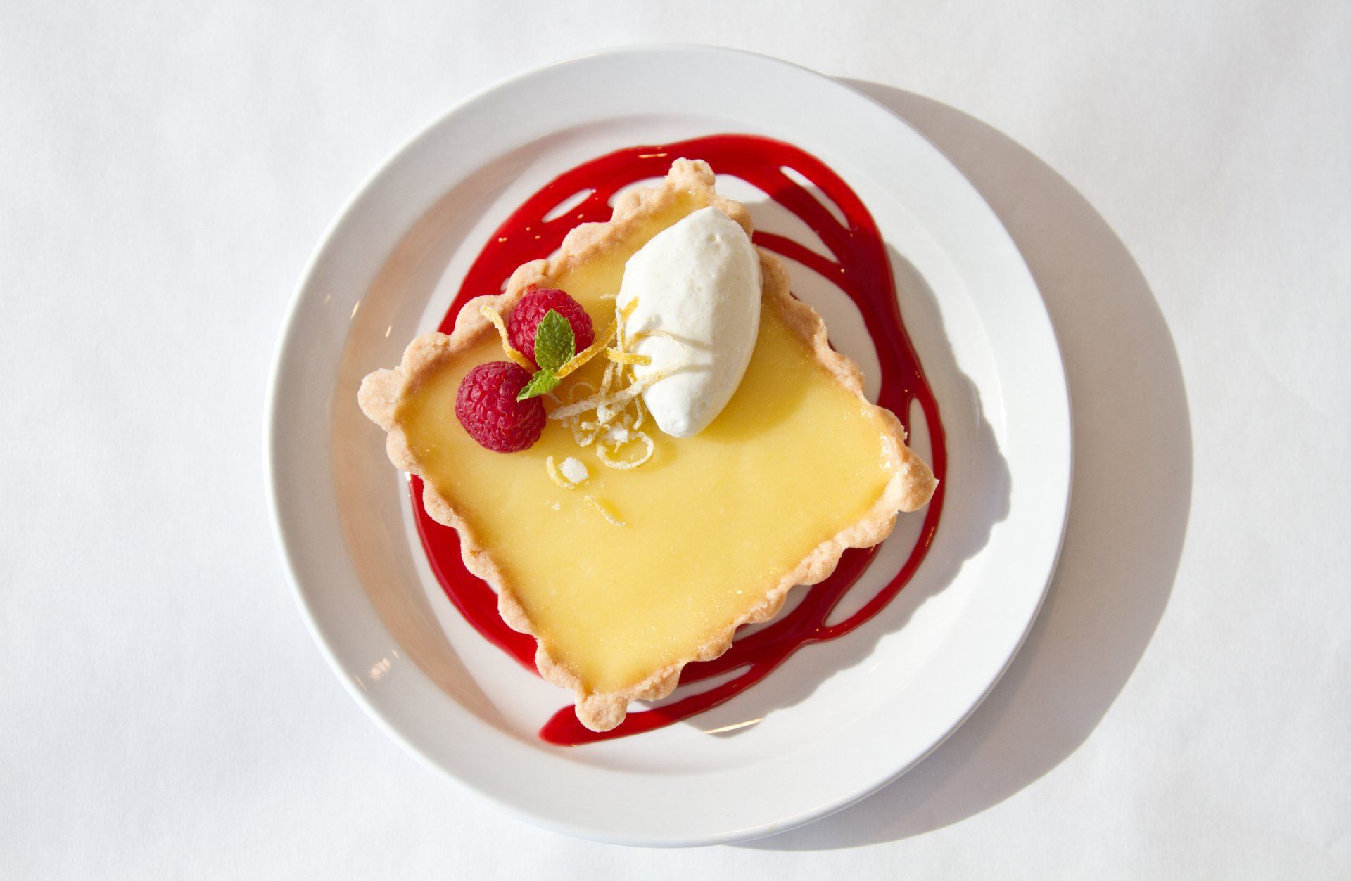Lemon tart with raspberry sauce, ice cream, and raspberries on a white plate.