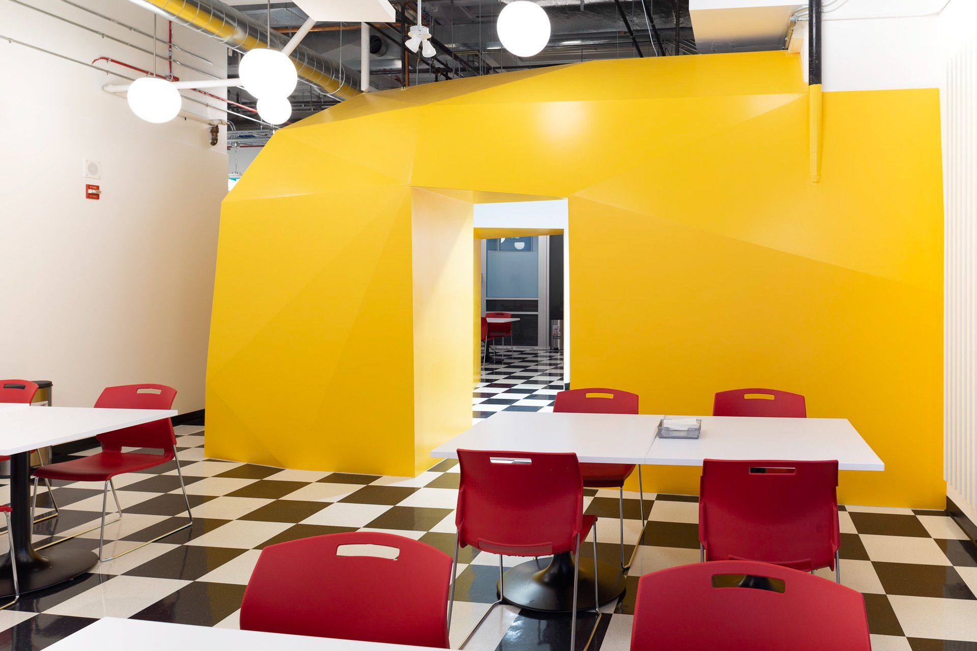 Yellow structure with doorway, tables, red chairs, and checkered floor.