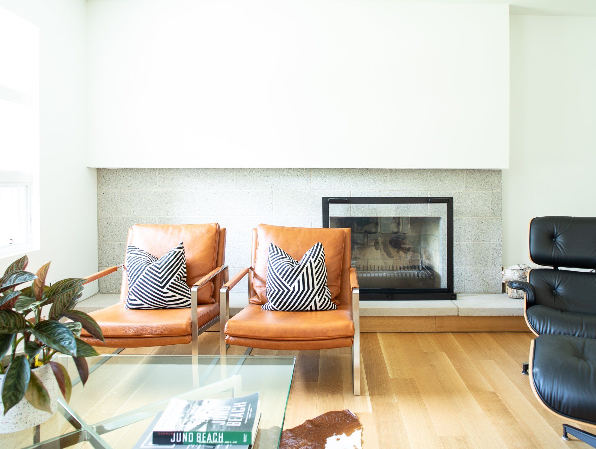Two brown leather chairs with black and white striped pillows in front of a fireplace.