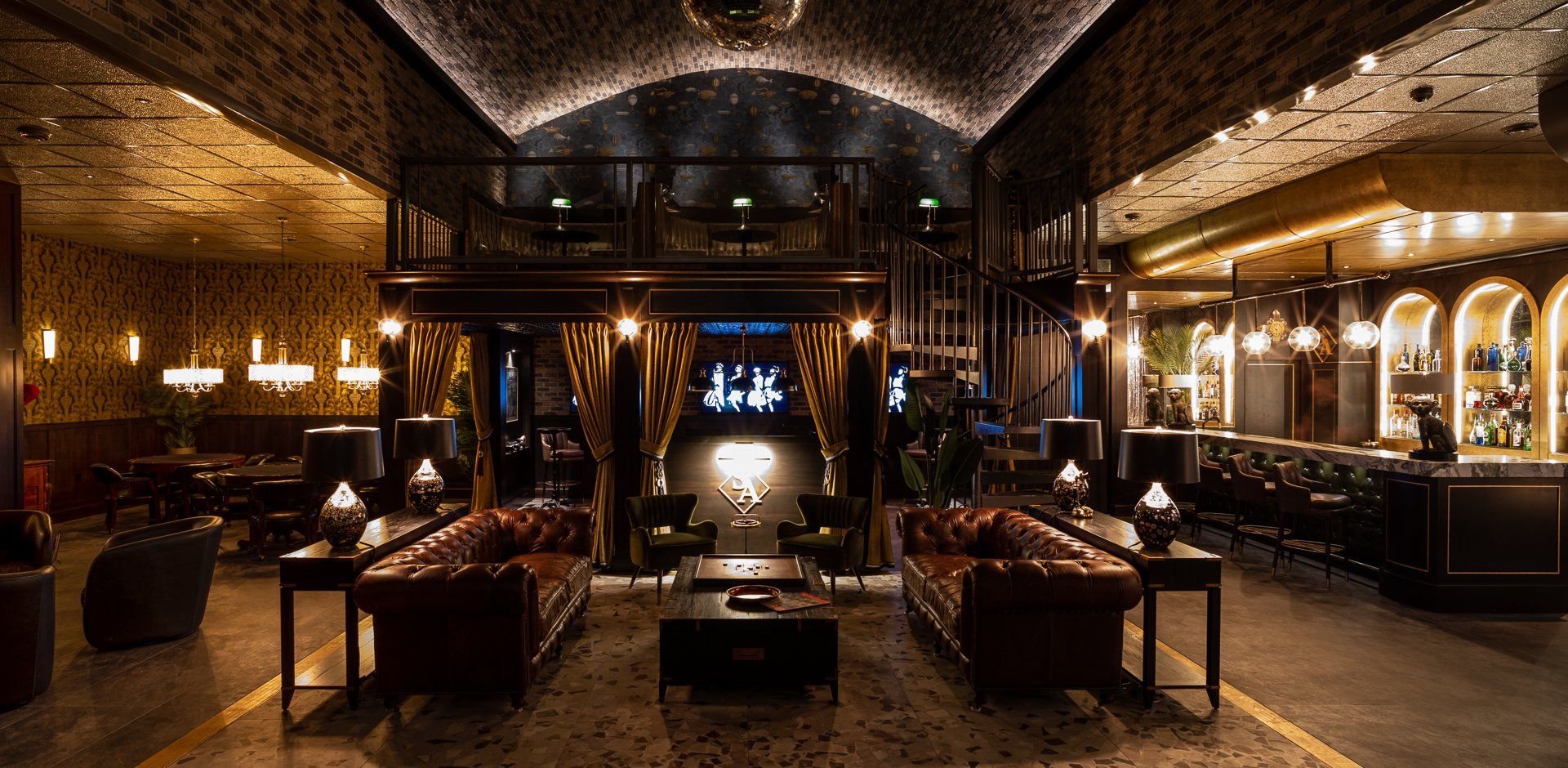 Luxurious dimly lit bar interior with Chesterfield sofas, bar, mezzanine level, and disco ball.