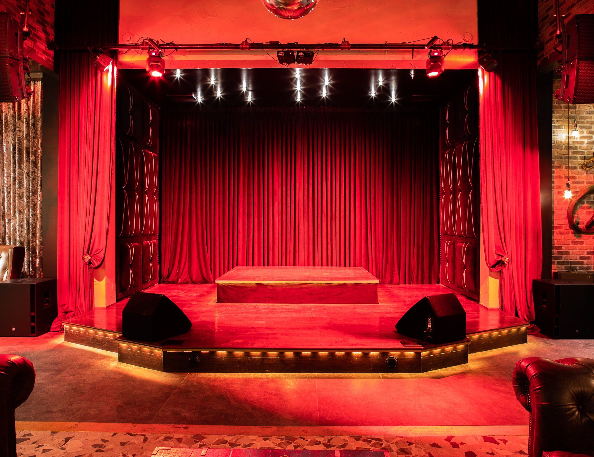 Red-lit stage with velvet curtains, spotlights, and speakers. Disco ball hangs above.
