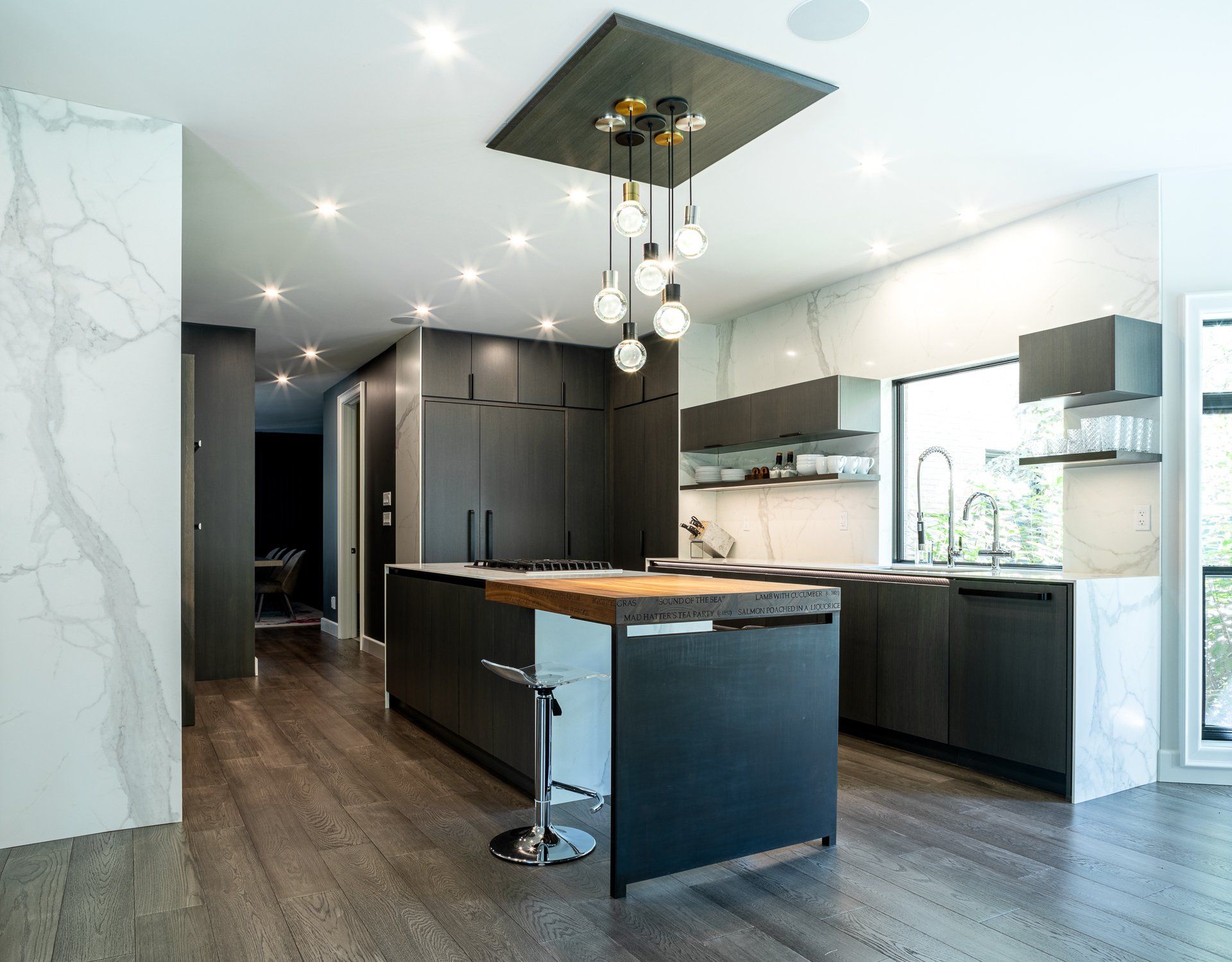 Modern kitchen with dark cabinetry, marble walls, wooden island countertop, and spherical light fixture.