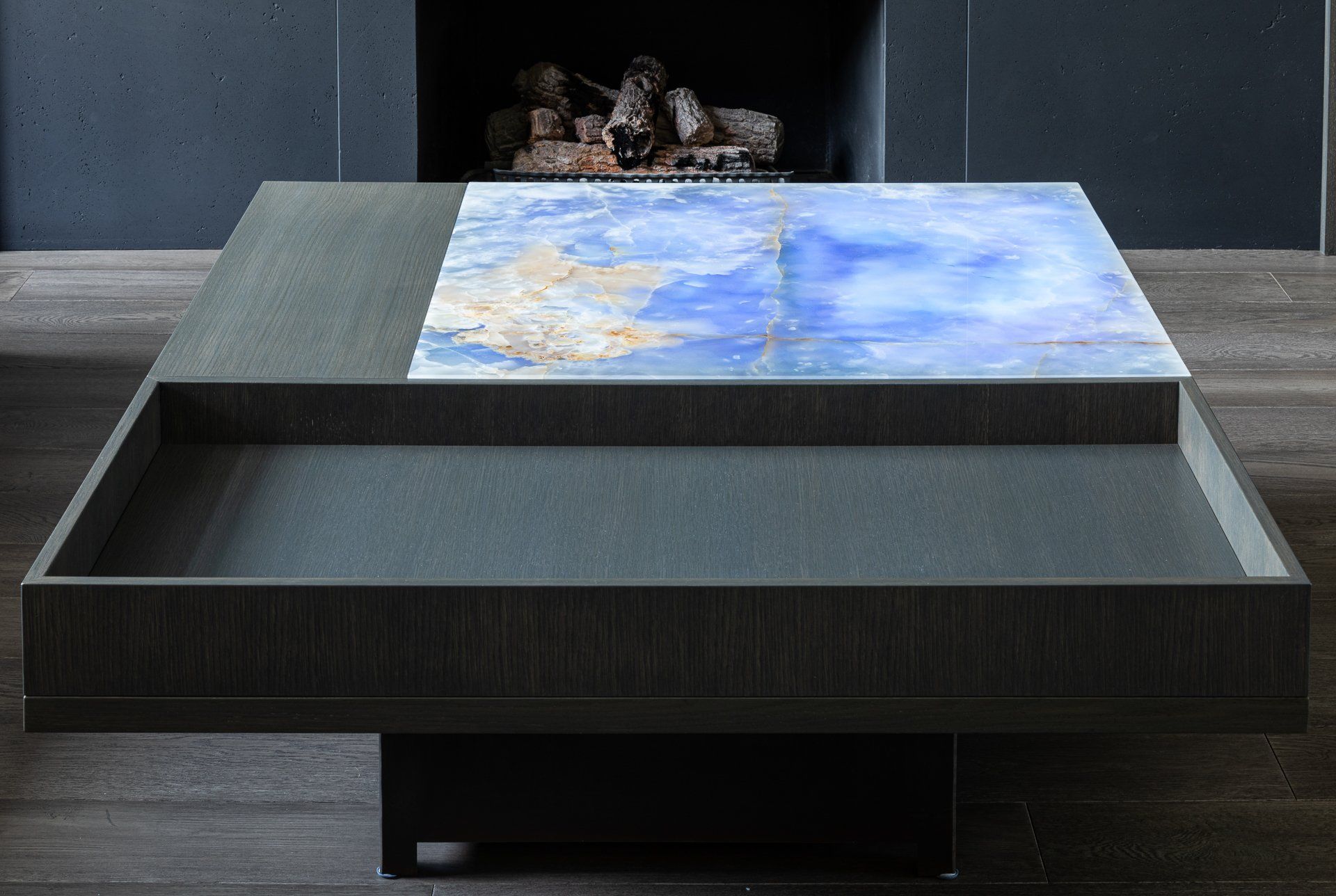 Modern square coffee table with blue stone inlay and tray detail, in front of a fireplace.