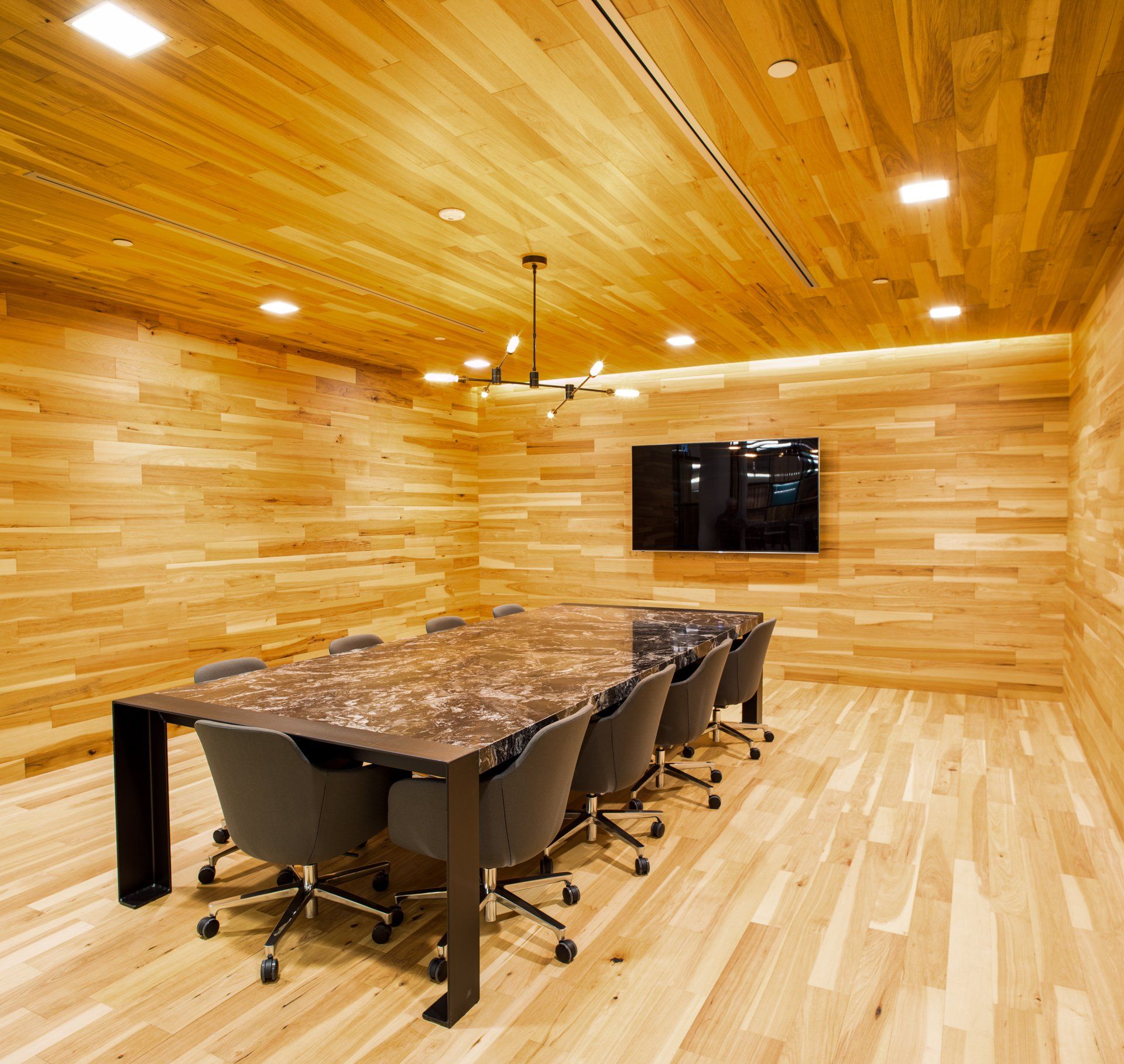 Wooden-paneled boardroom with large table, chairs, TV, and ceiling lights.