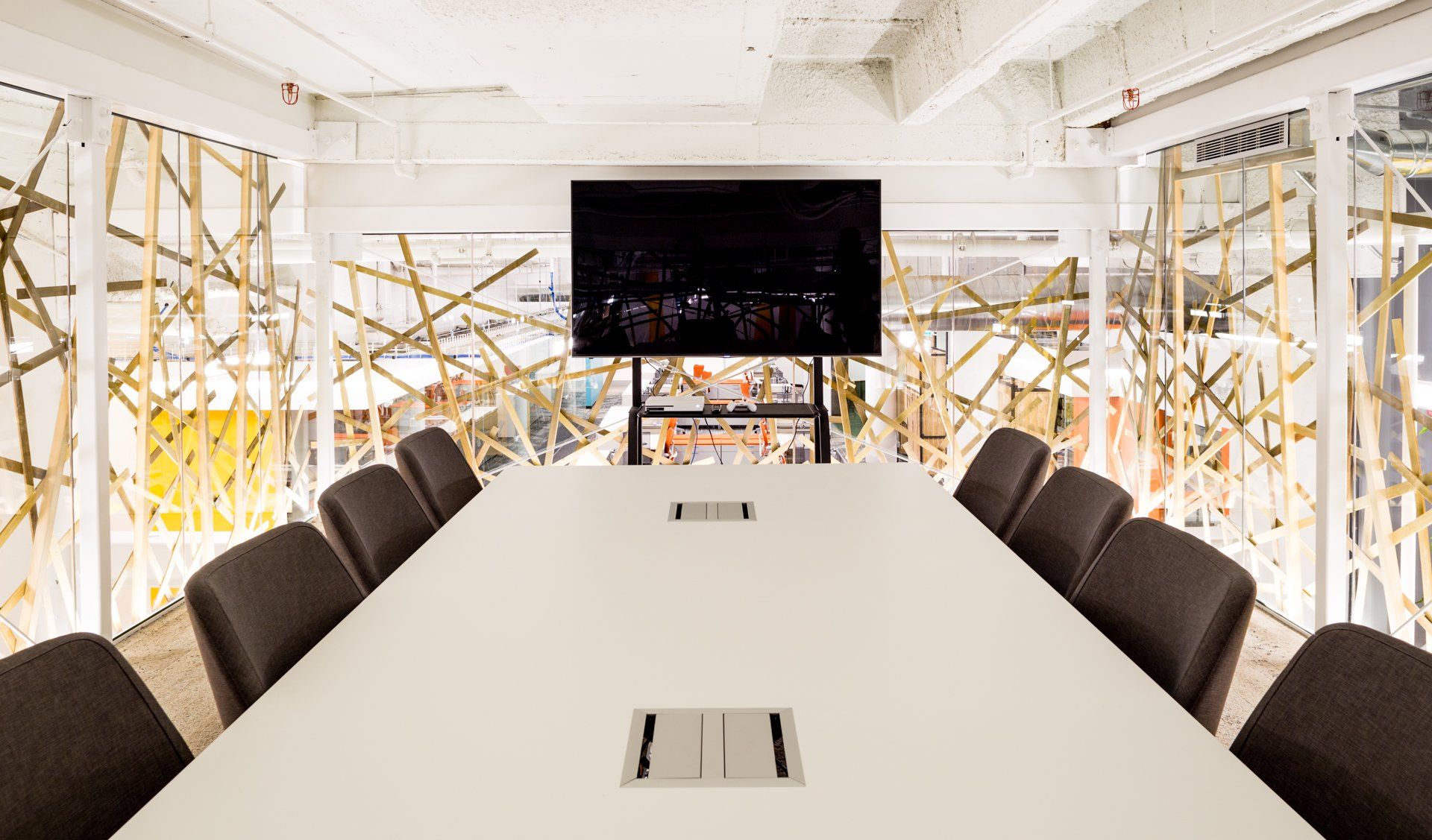 Conference room with long white table, chairs, large TV, and decorative gold wall accents.