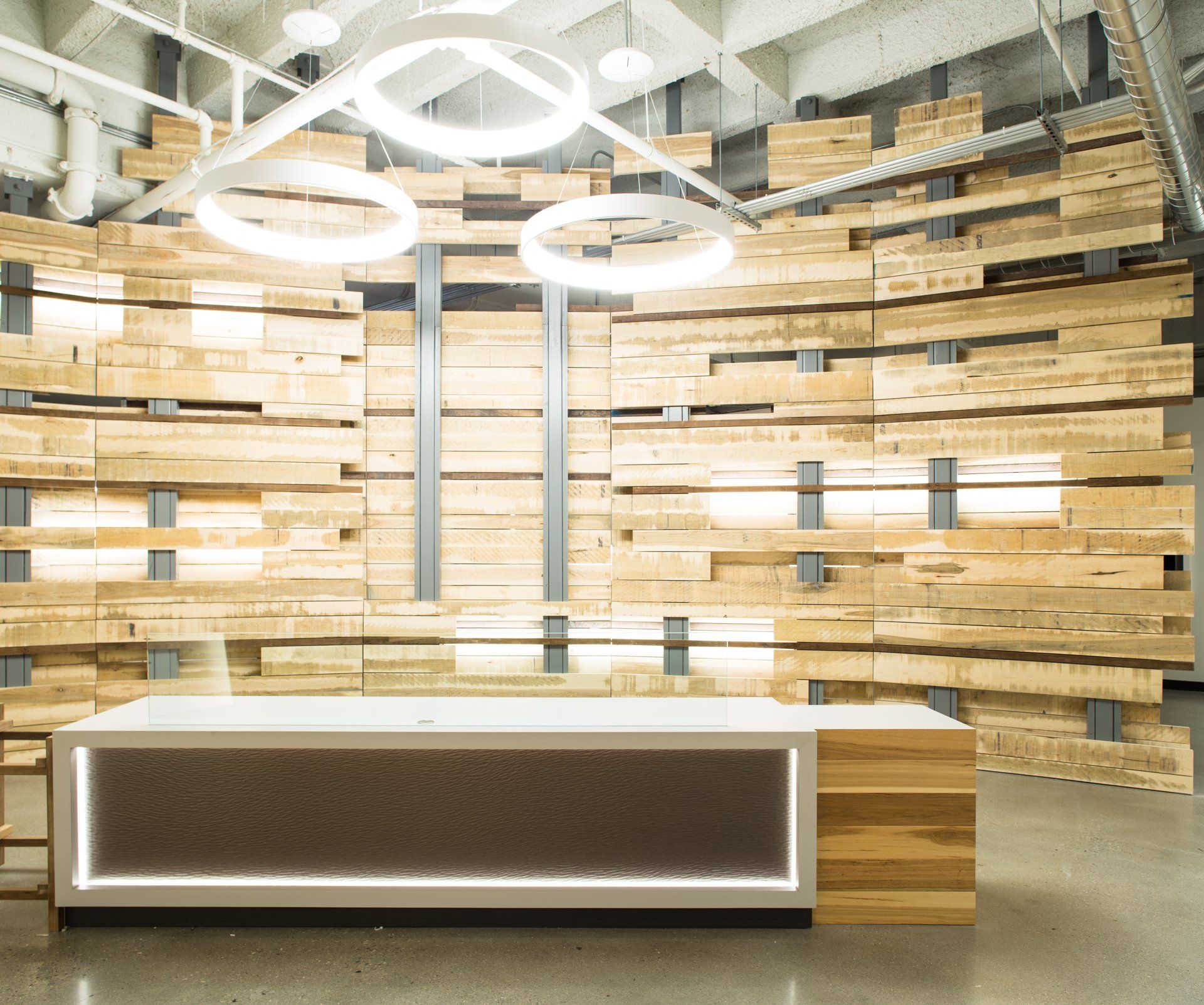 Reception area with a wooden plank wall, white desk, and circular lights.