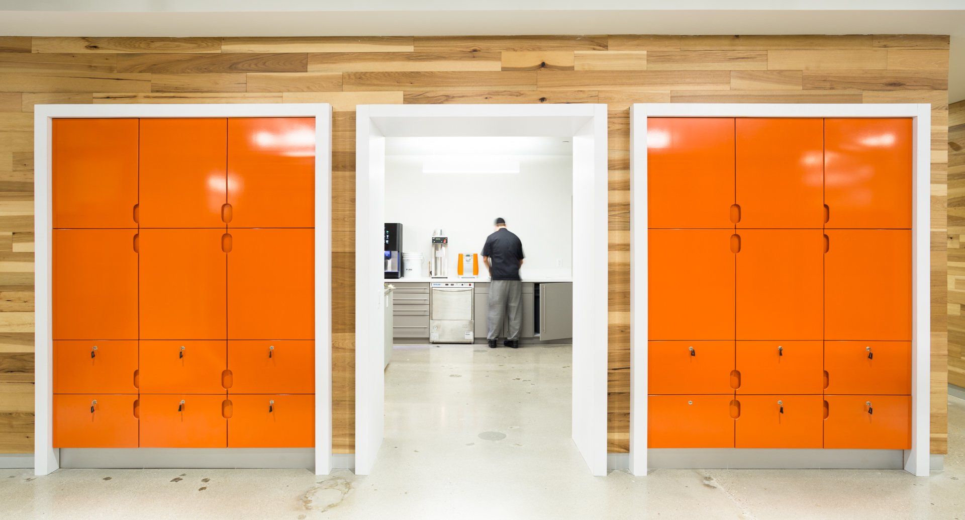 Three orange lockers with white frames, wood paneling background. A person stands in the open doorway.