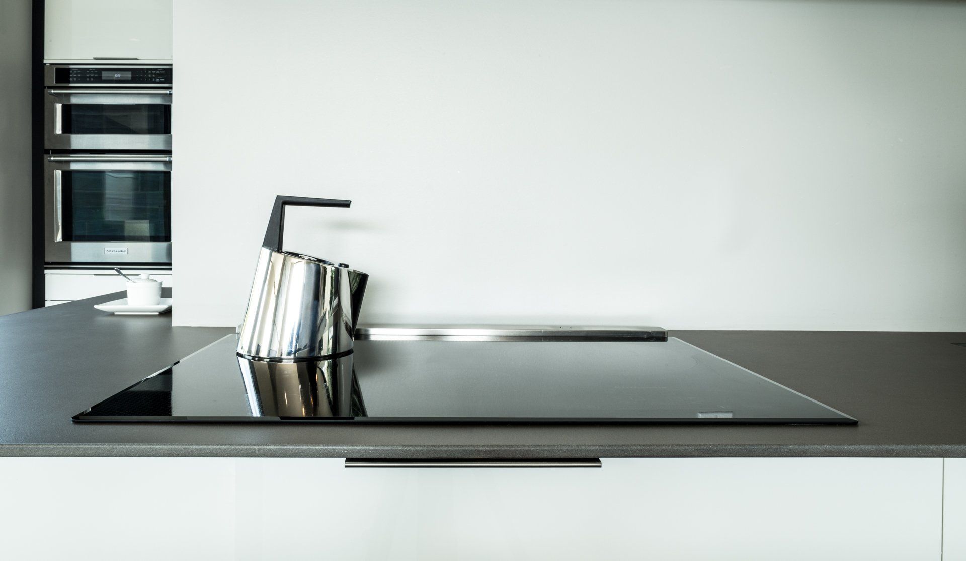 A stainless steel kettle on a black cooktop in a modern white kitchen.