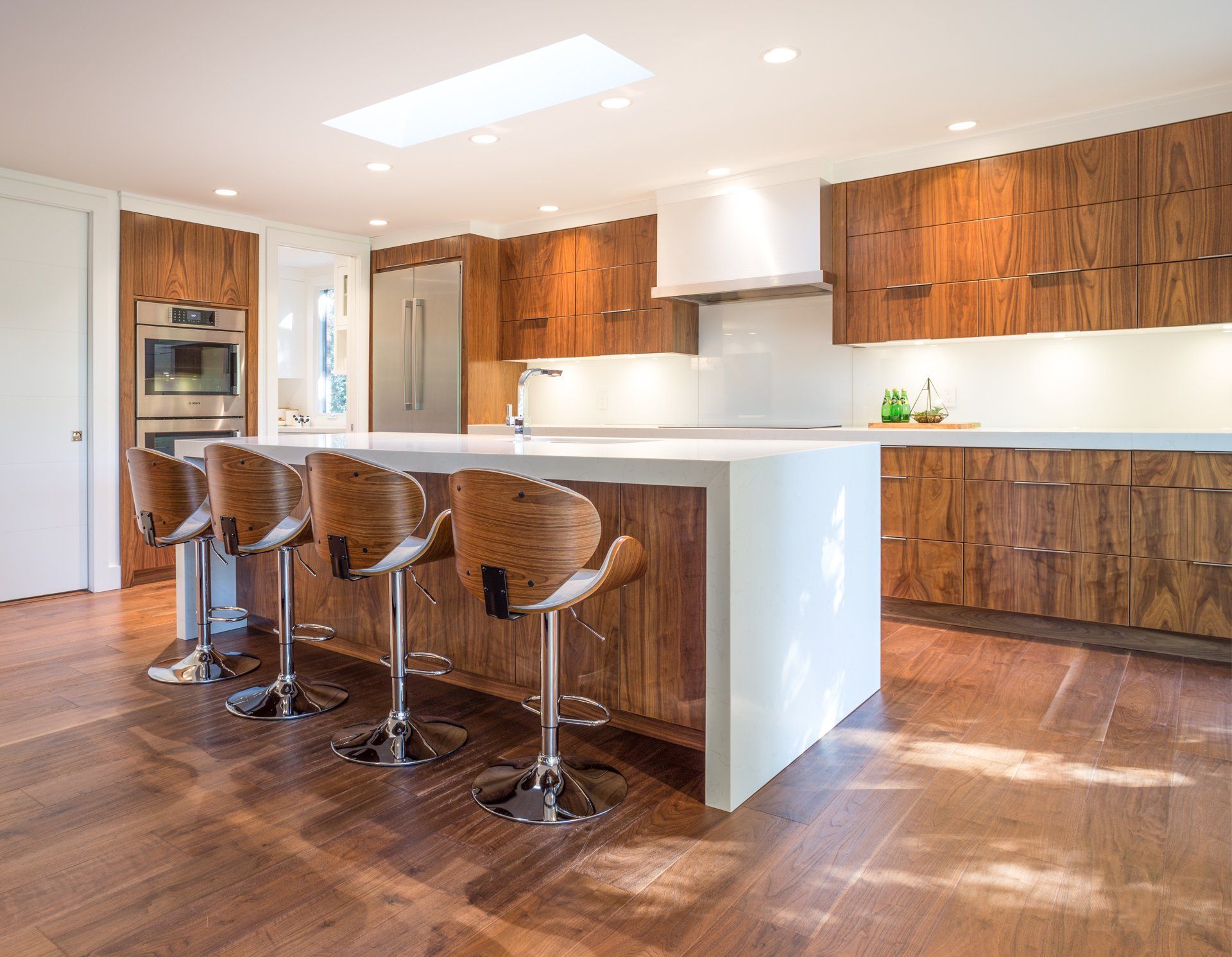 Modern kitchen with wood cabinets, white countertops, island with bar stools, and wood flooring.