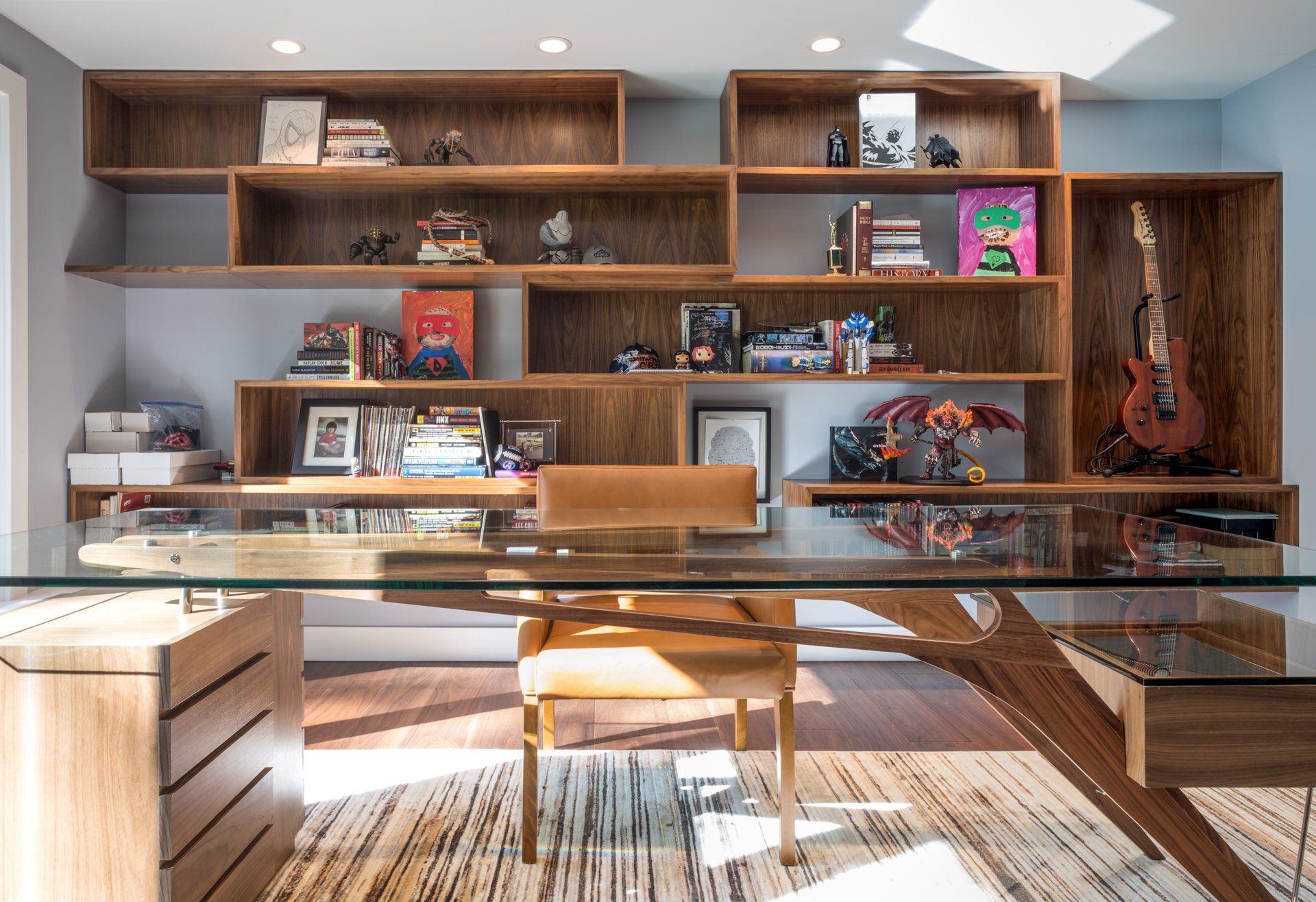 Office space with wooden shelving displaying books and collectibles, a glass desk, and a wooden chair.