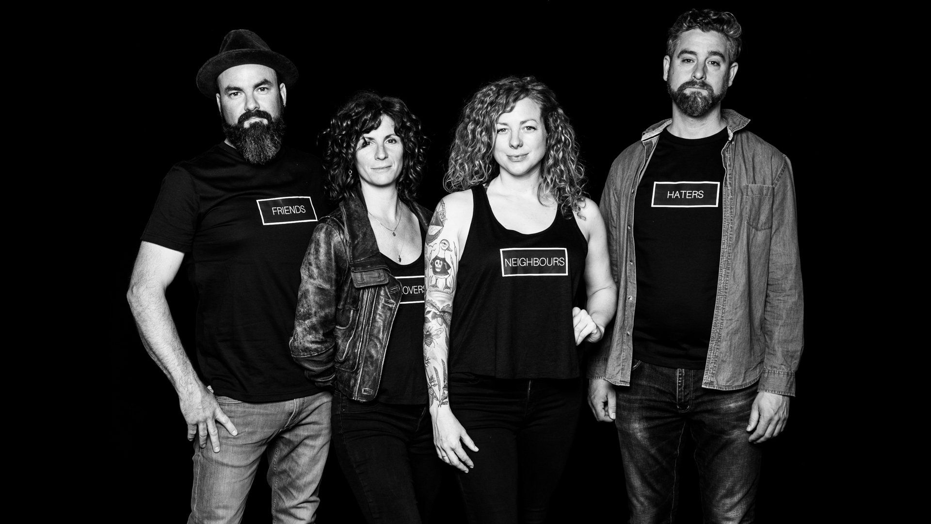 Four people posing in front of a dark background. All are wearing shirts that read 
