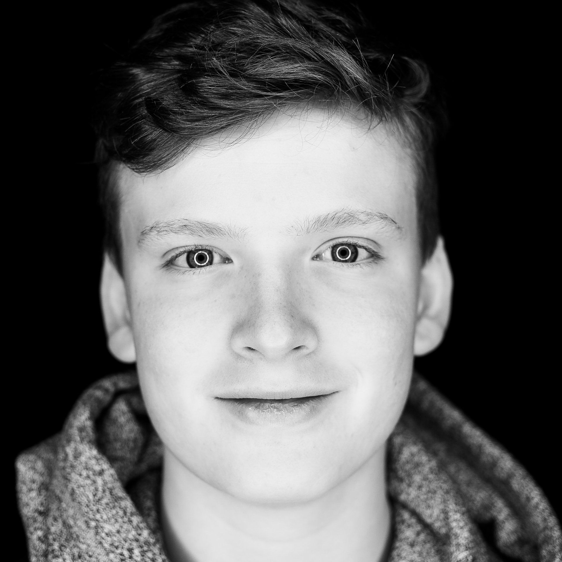 Smiling person in gray hoodie against a black background.