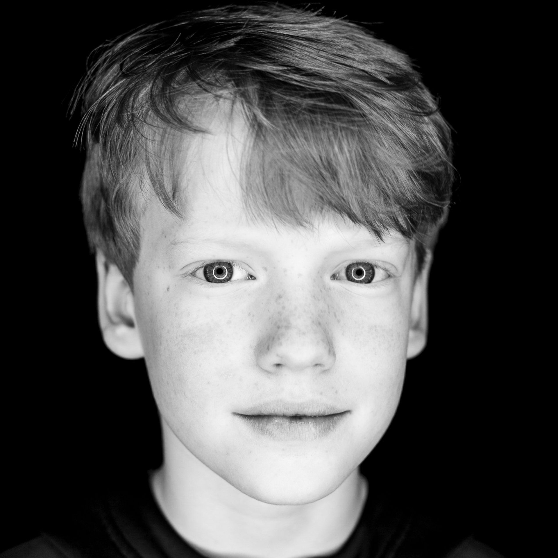 Young person with fair skin and freckles, looking at the camera. Black and white portrait with dark background.