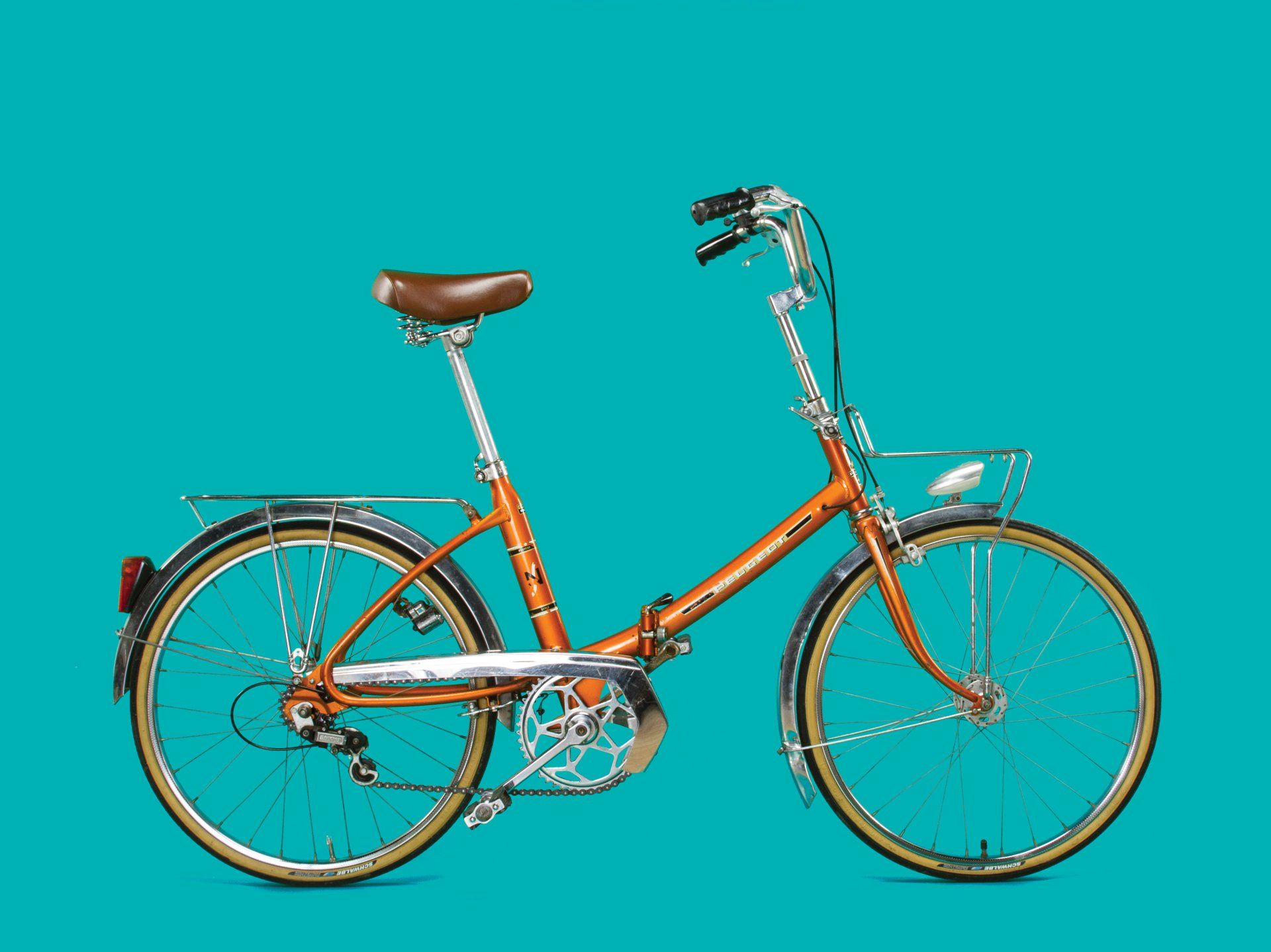 Orange folding bicycle with chrome accents and a basket, set against a teal background.