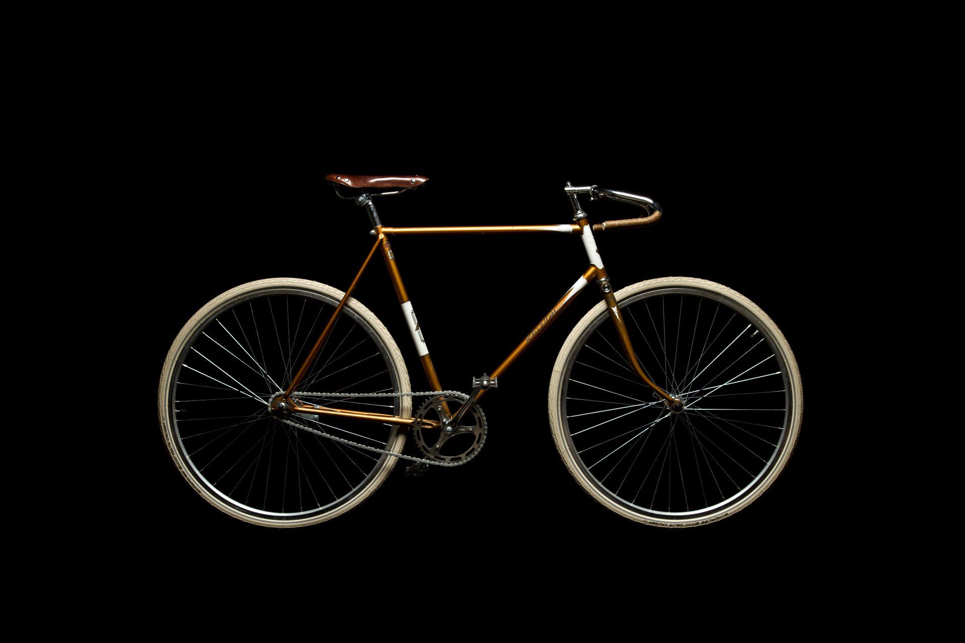 Bronze-colored vintage bicycle with white tires against a black background.