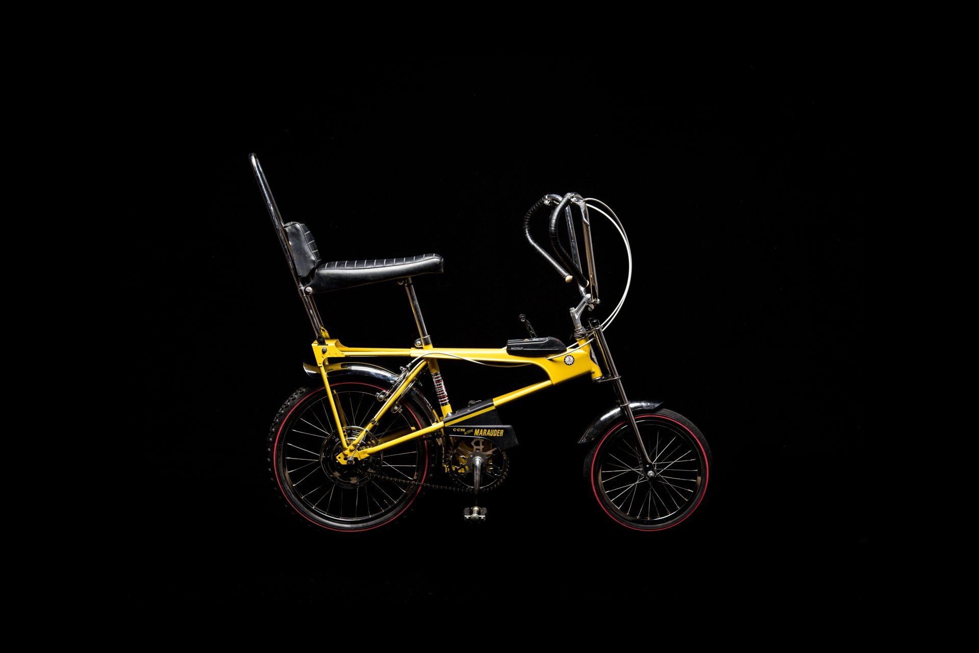 Yellow and black Stingray bicycle with a tall backrest and curved handlebars.