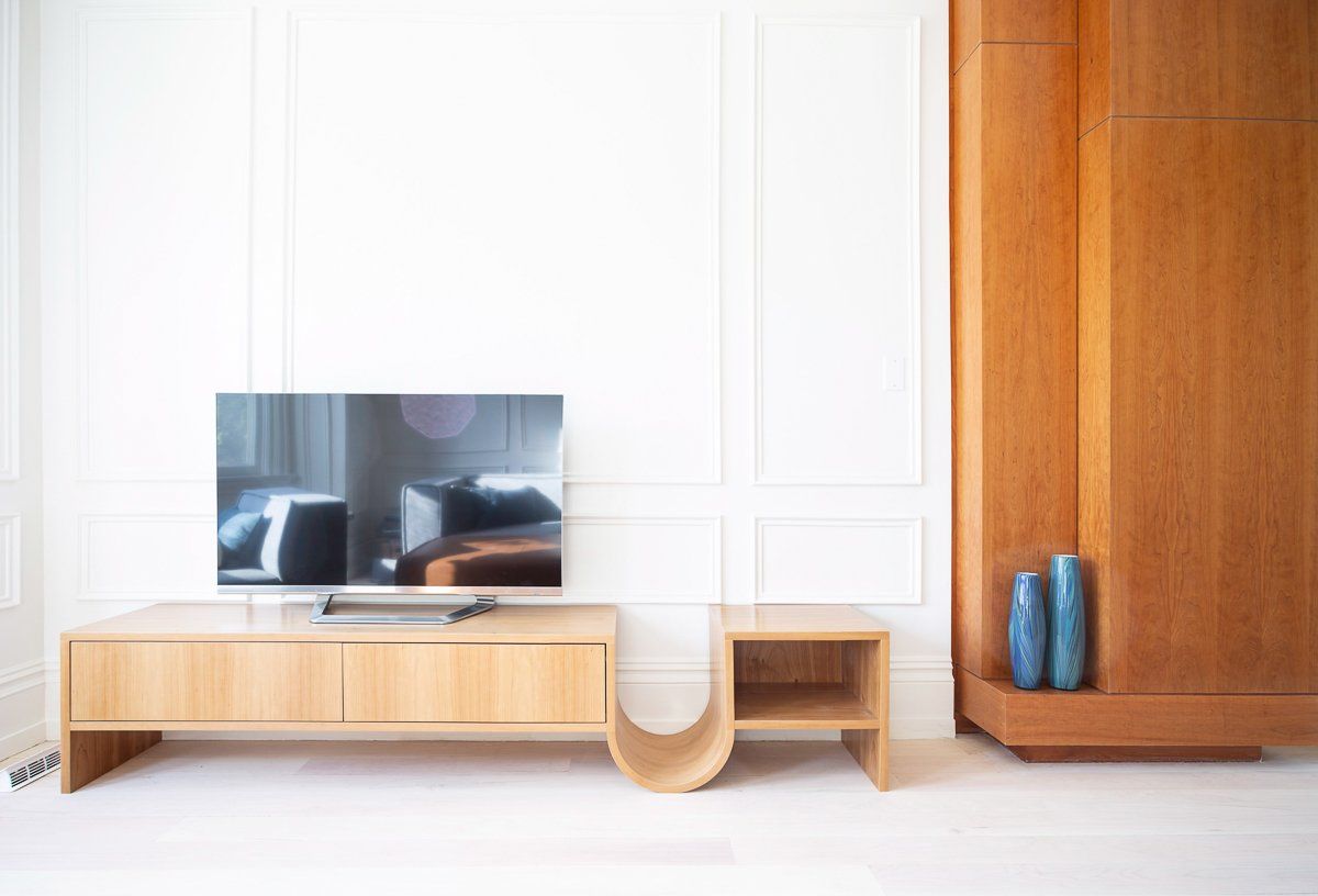Living room with light wood TV console, flat-screen TV, and decorative vases near a wood panel cabinet against a white wall.