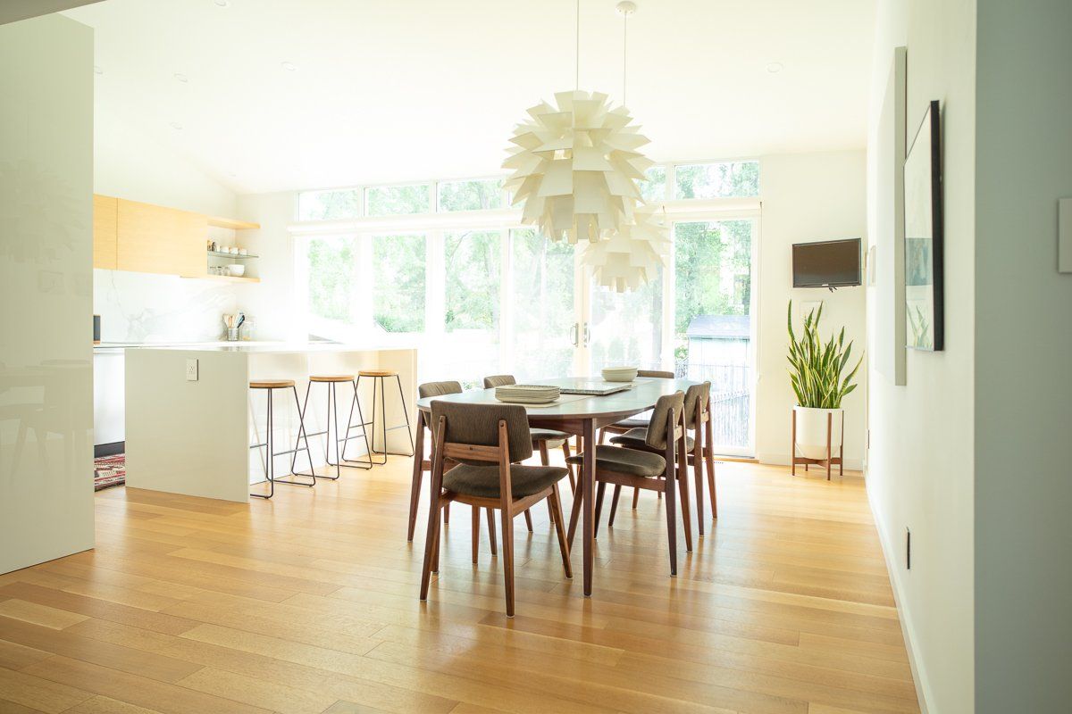 Dining room with a table, chairs, and a large white light fixture. Kitchen in background.