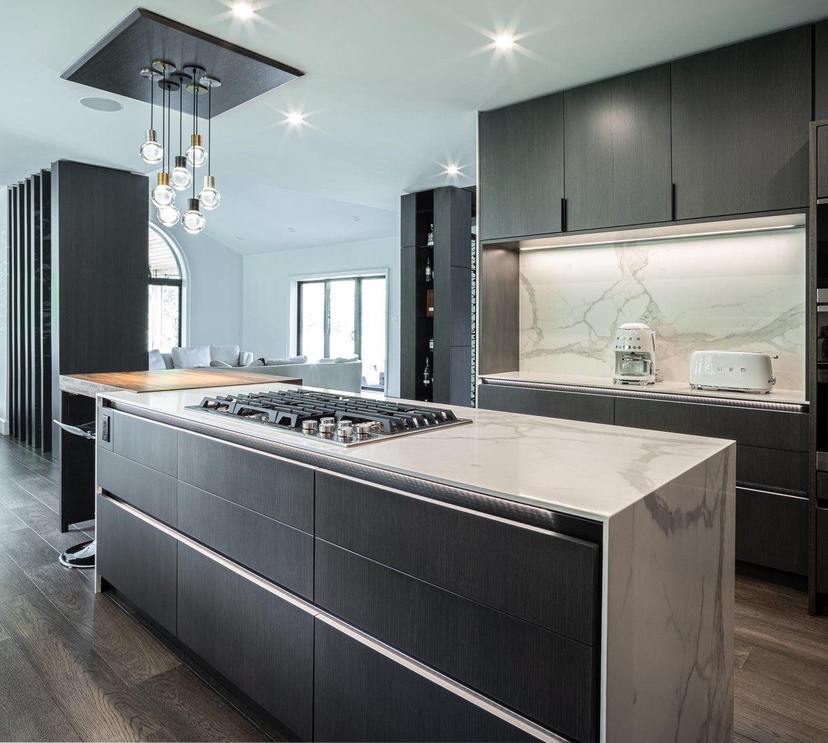 Modern gray kitchen with island, cooktop, and marble countertops, with overhead light fixture.