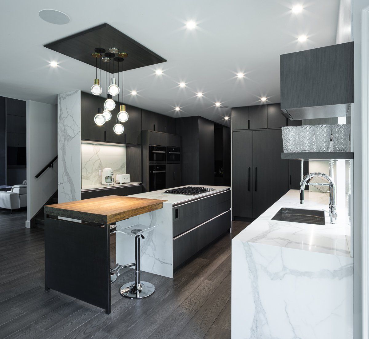Modern black kitchen with marble countertops, wood flooring, and island with a butcher block and seating.