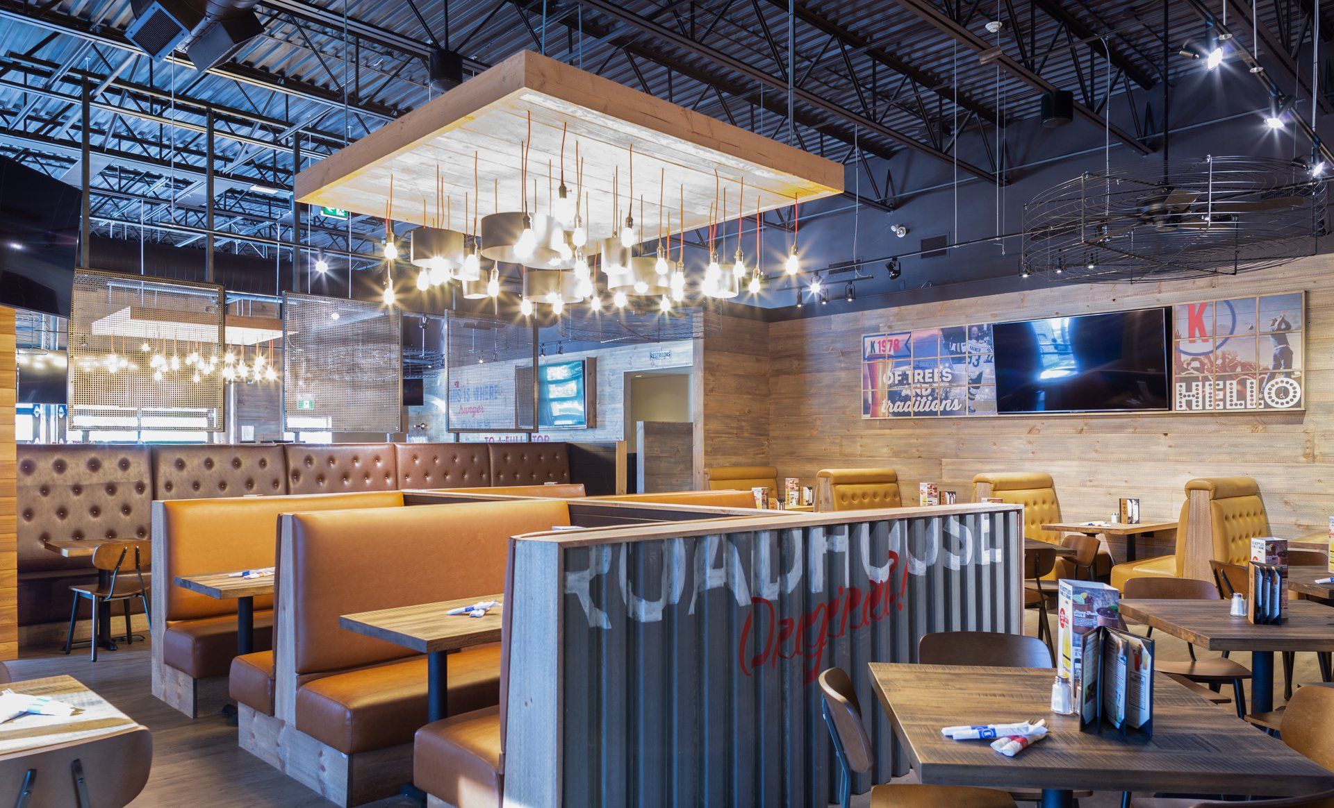 Restaurant interior with booths and tables, featuring industrial-chic design: brick walls, metal accents, and a large light fixture.