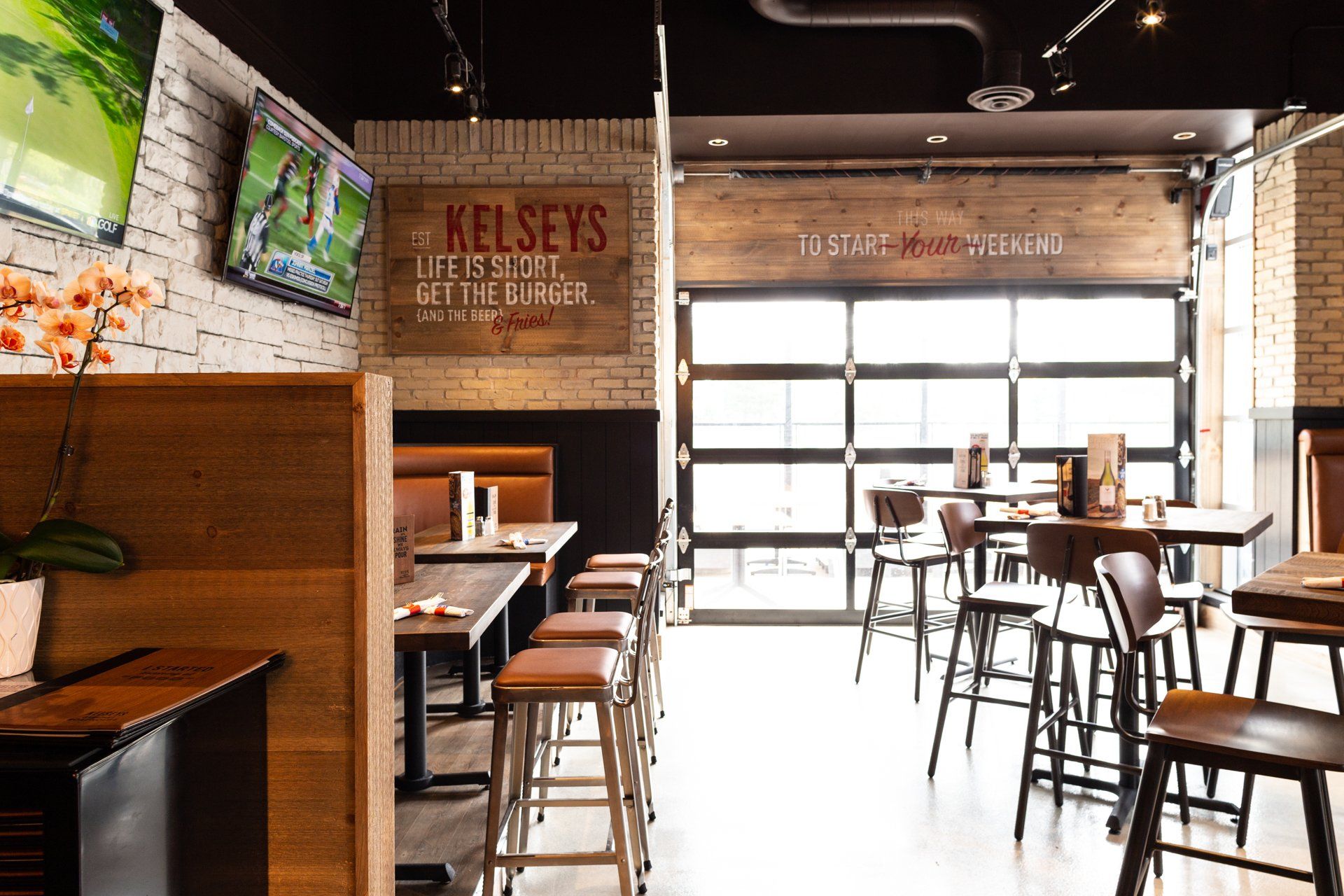 Interior of Kelsey's restaurant with tables, stools, TVs, and a large door.