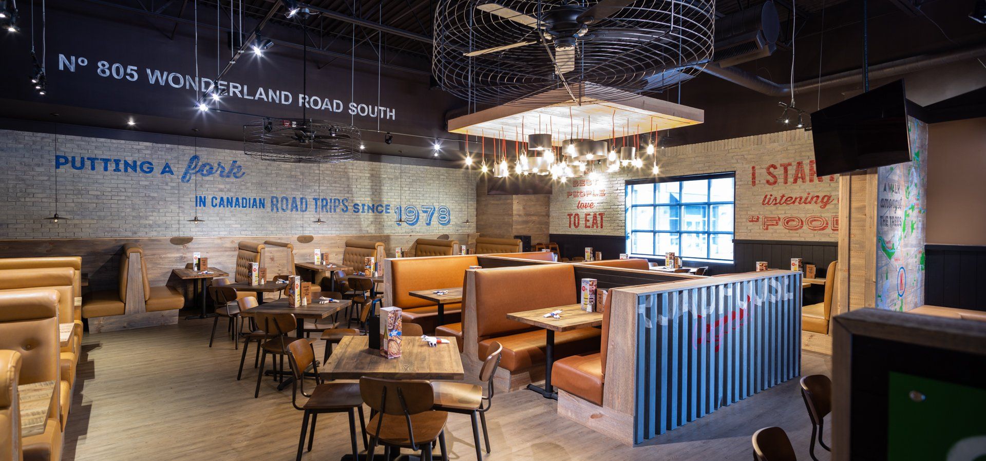 Interior of a restaurant with booths and tables.  A decorative light fixture hangs from the ceiling. Brick walls and dark accents.