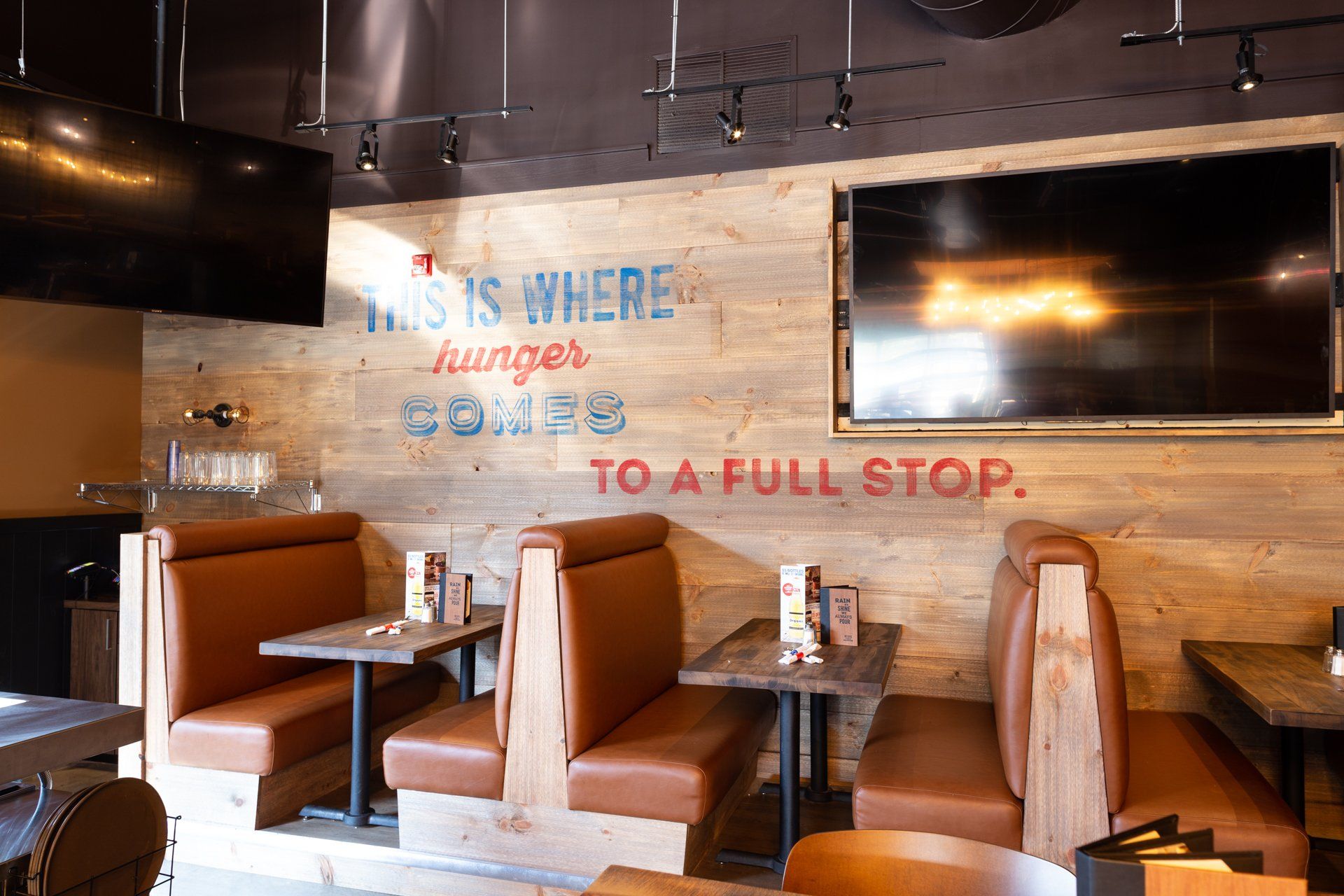Restaurant interior with wood-paneled walls, booths, tables, a TV, and a sign that reads, 