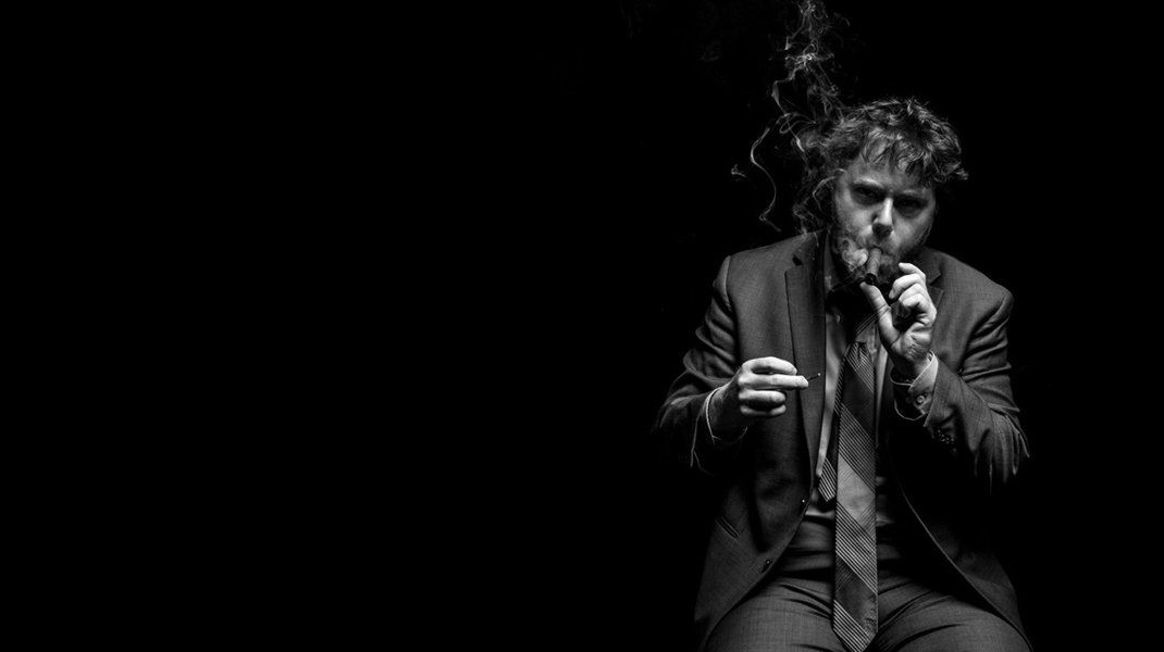 Man in suit smoking, smoke rising, black background.