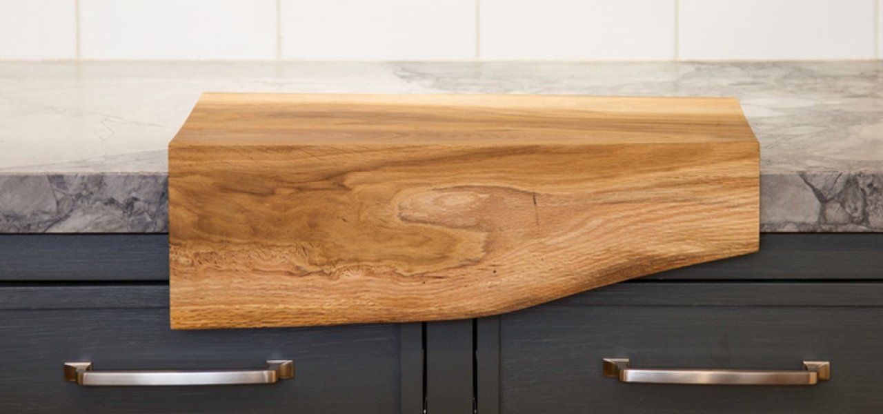 Wooden cutting board on a countertop above dark cabinets with silver handles.