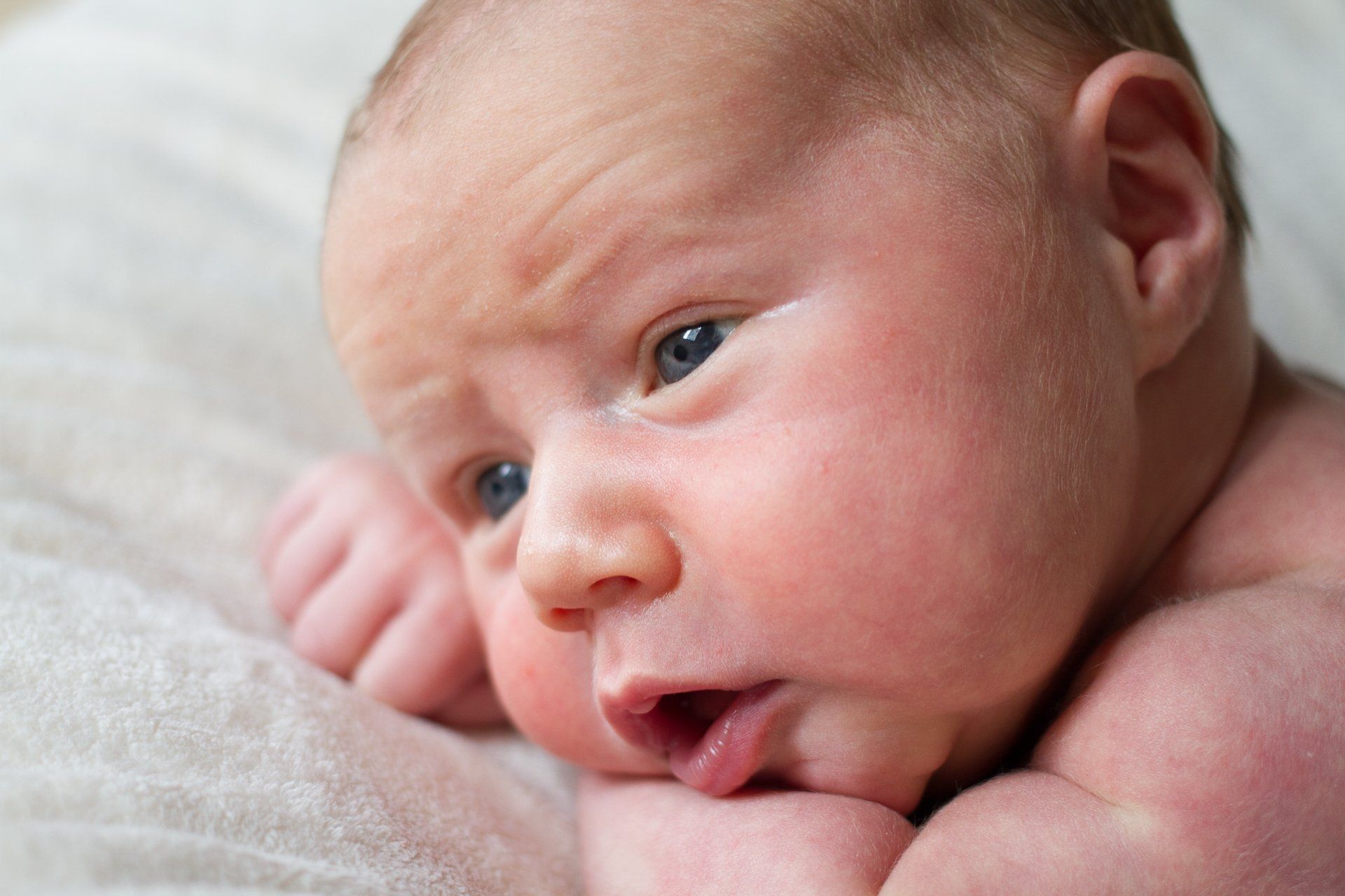 Newborn baby with blue eyes, resting on a white blanket.