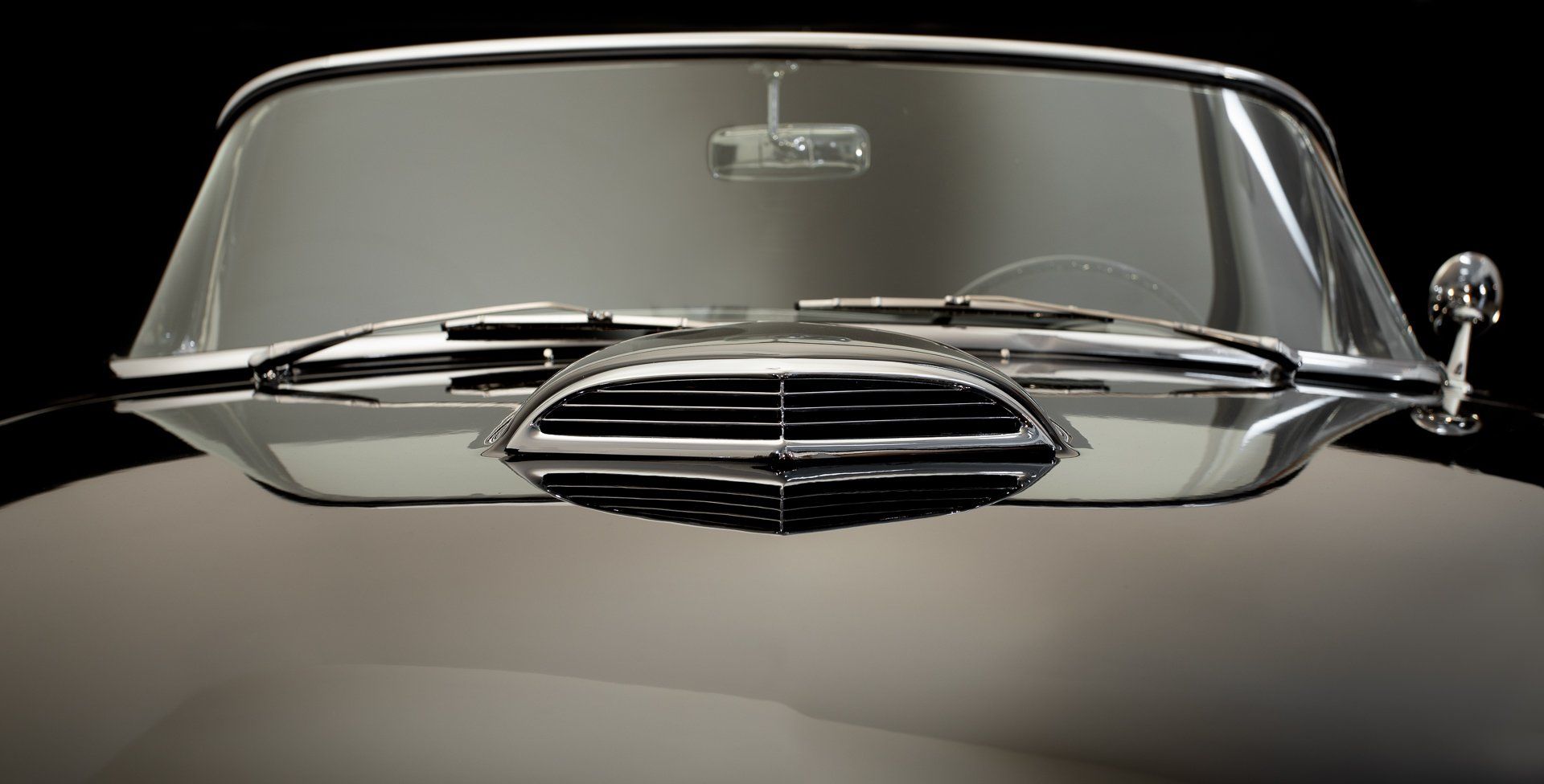 Close-up of a classic car's front with chrome grill and windshield against a dark background.