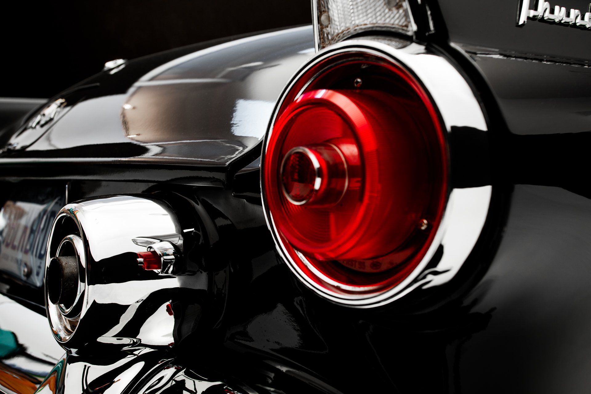 Close-up of a classic black car's taillight with a red center and chrome detailing.