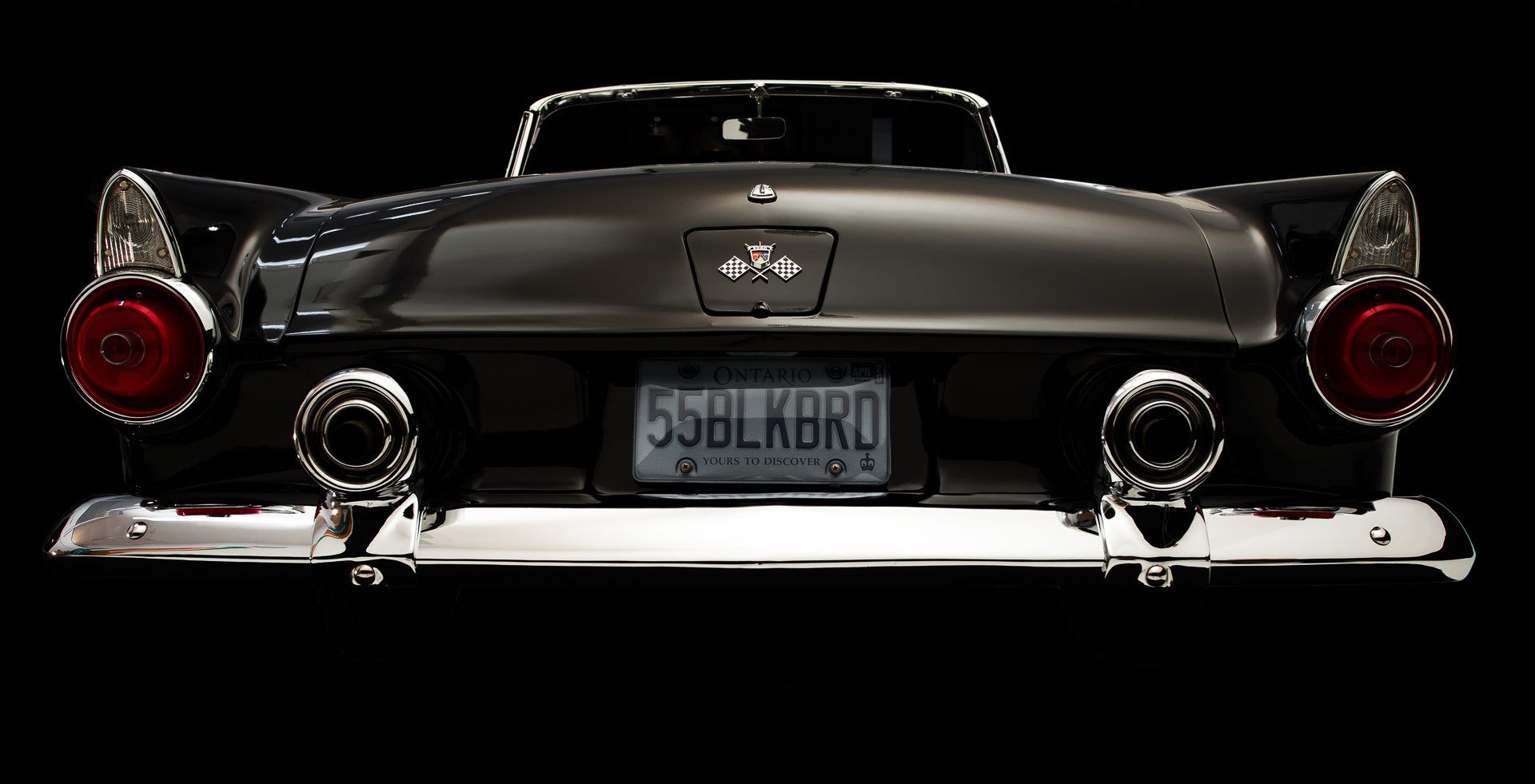 Rear view of a classic black car with chrome accents and round taillights; license plate reads 