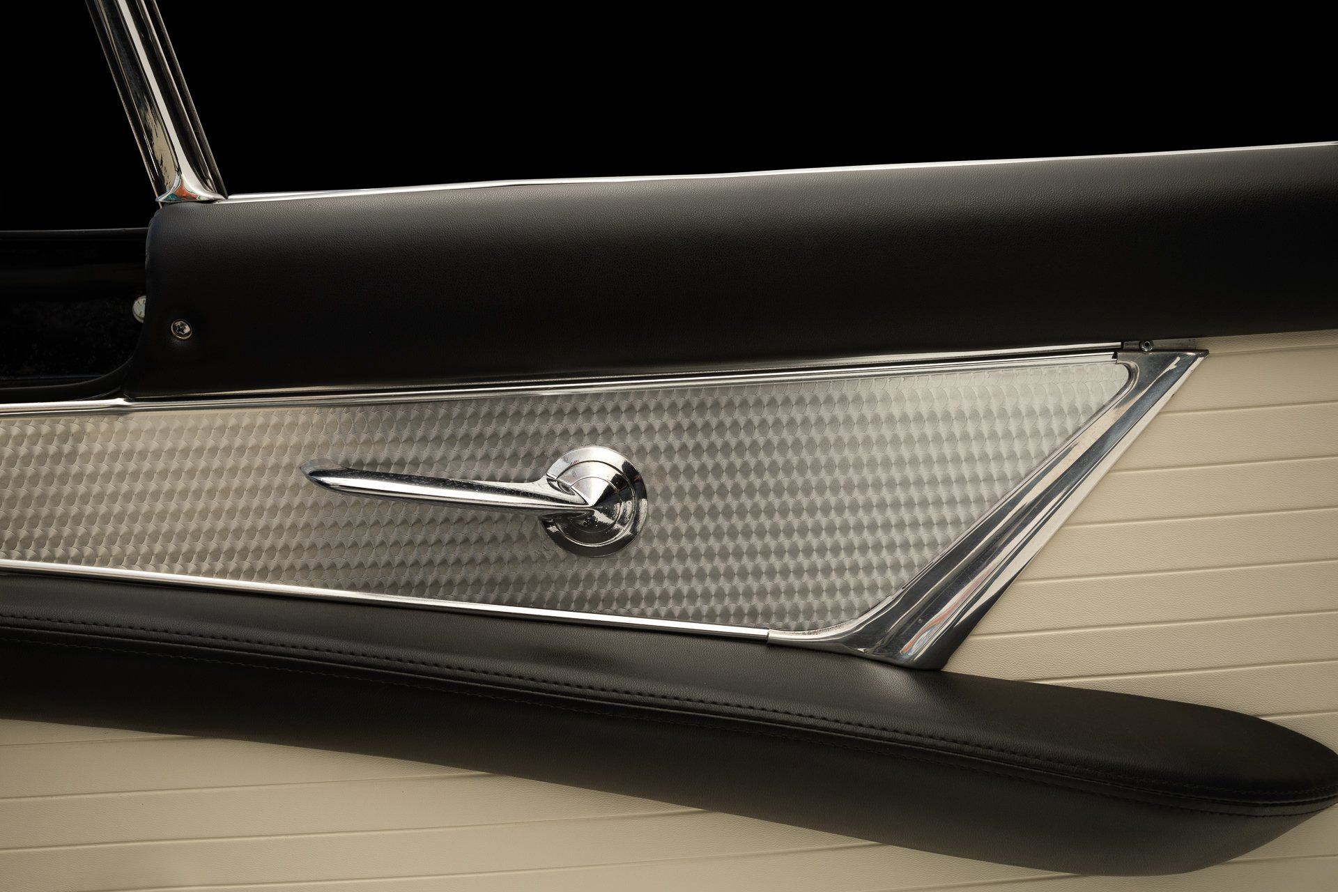 Close-up of a classic car door panel. Beige and black with chrome handle.