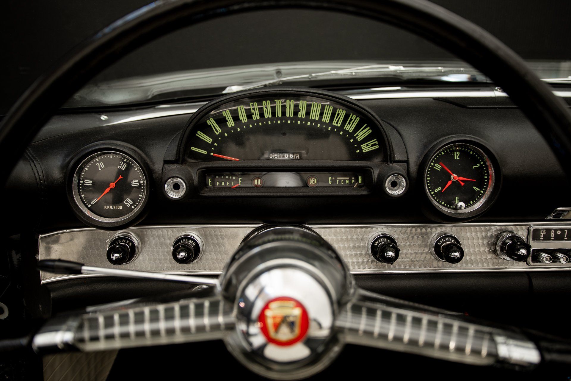 Dashboard of a classic black car with silver accents; speedometer, gauges, and steering wheel visible.