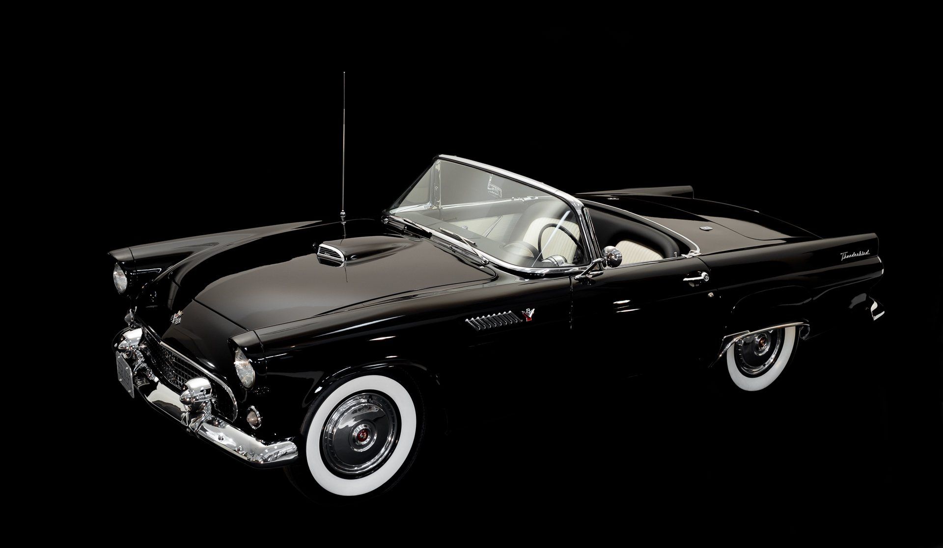 Black classic Ford Thunderbird convertible. White-wall tires, chrome accents, against a black background.