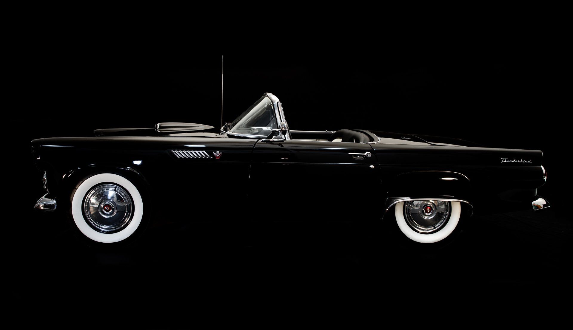 Black convertible car with white wall tires against a black background.