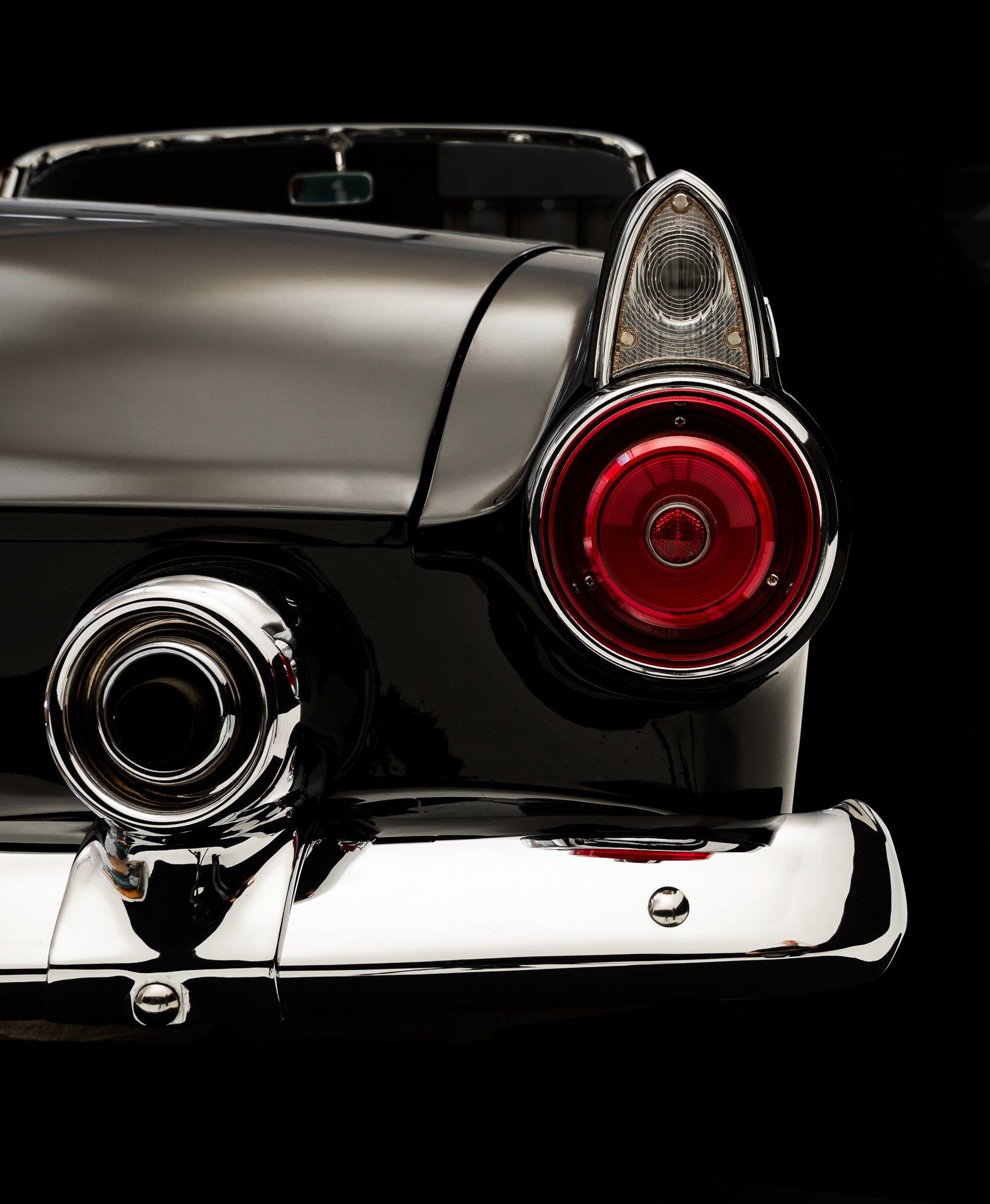 Black and silver classic car rear end detail, red taillight.