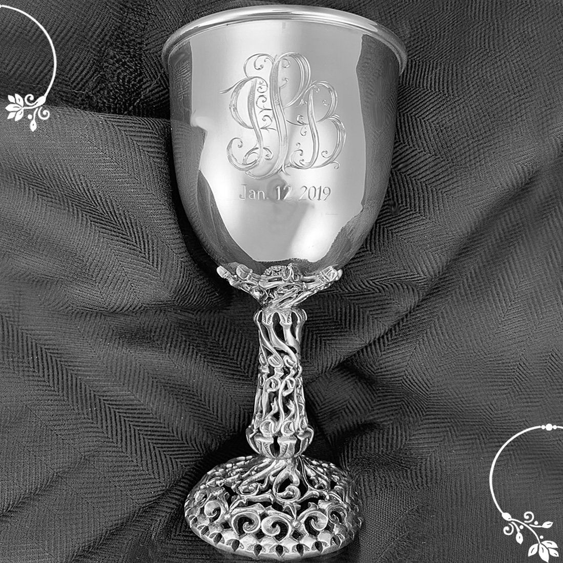 A silver goblet with a monogram on it is sitting on a table.
