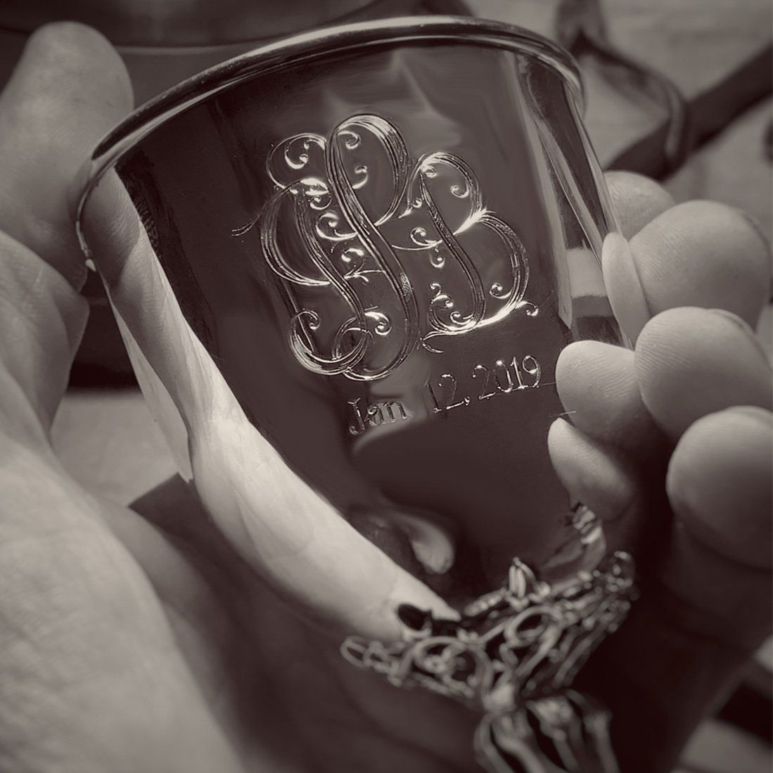 A black and white photo of a person holding a cup with a monogram on it