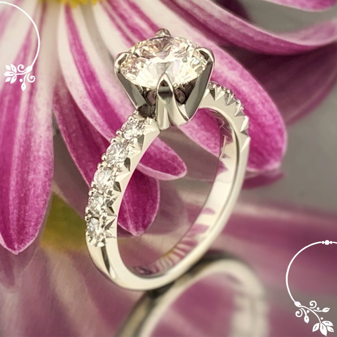 A close up of a diamond ring in front of a pink flower