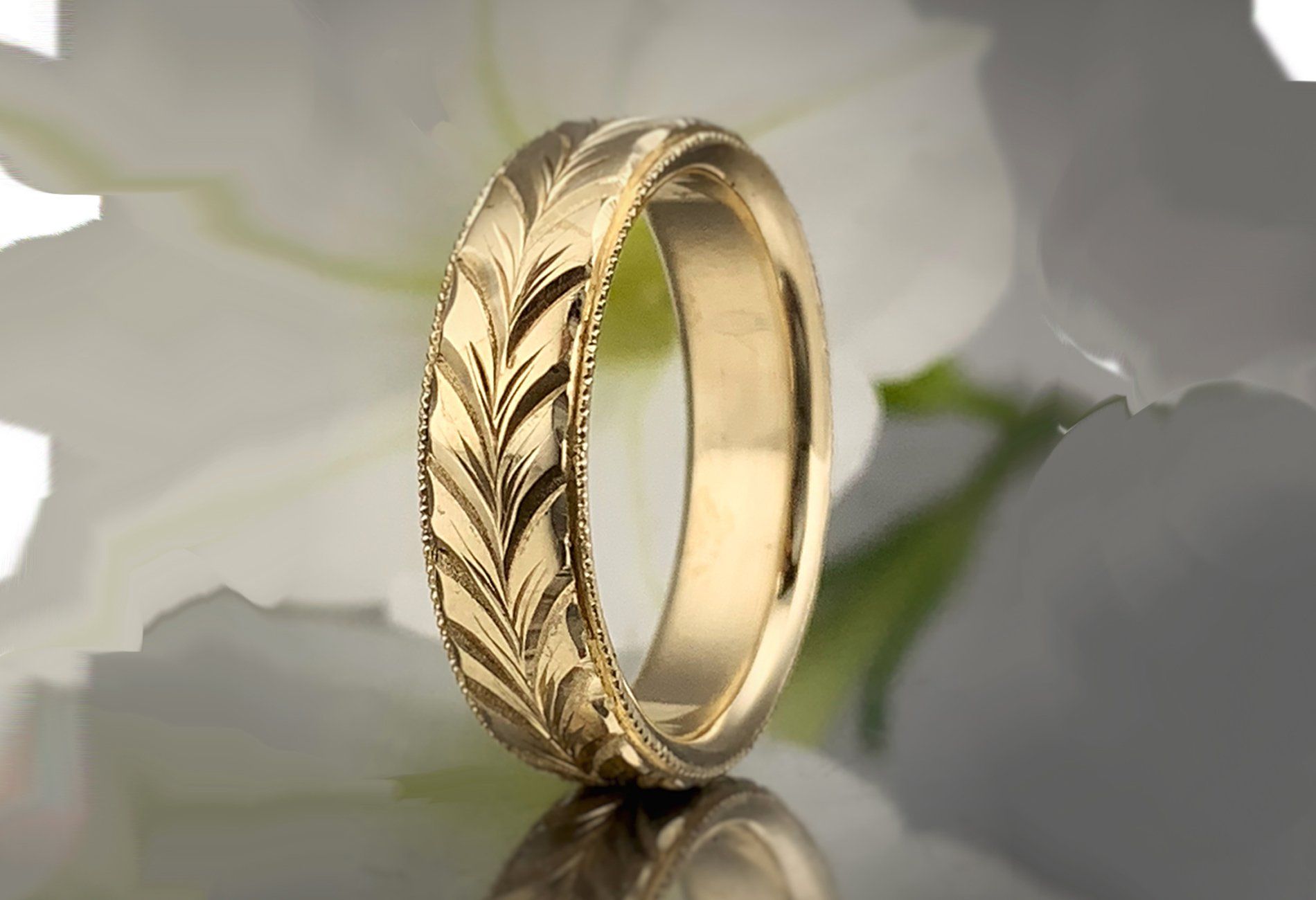 A gold ring is sitting on a table in front of a flower.