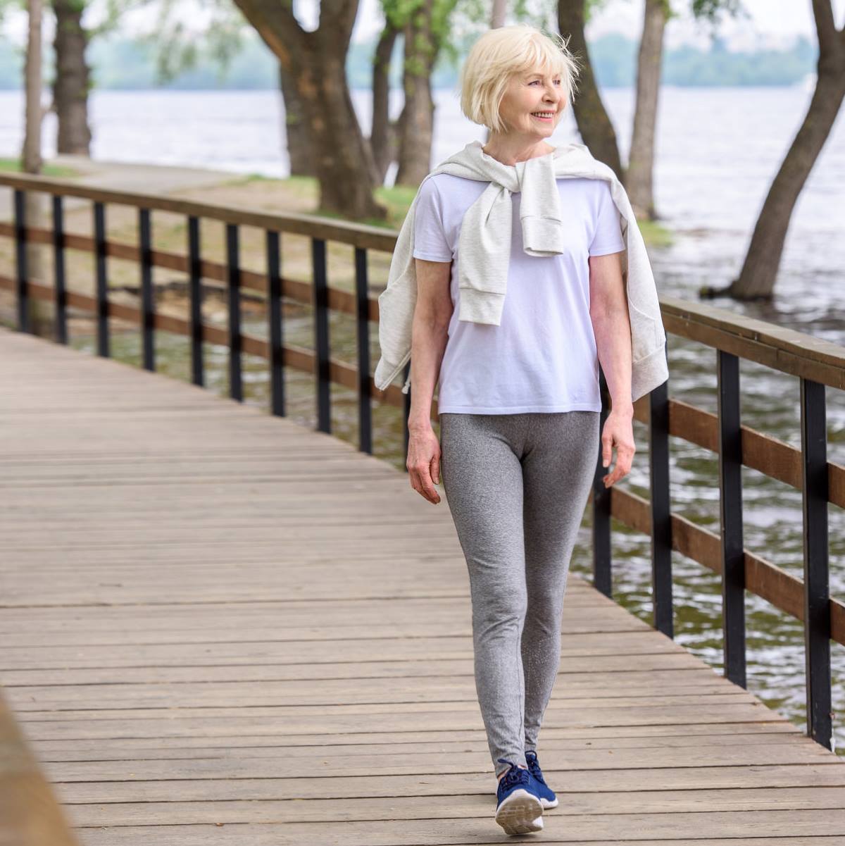 A woman is walking on a wooden bridge over a body of water.