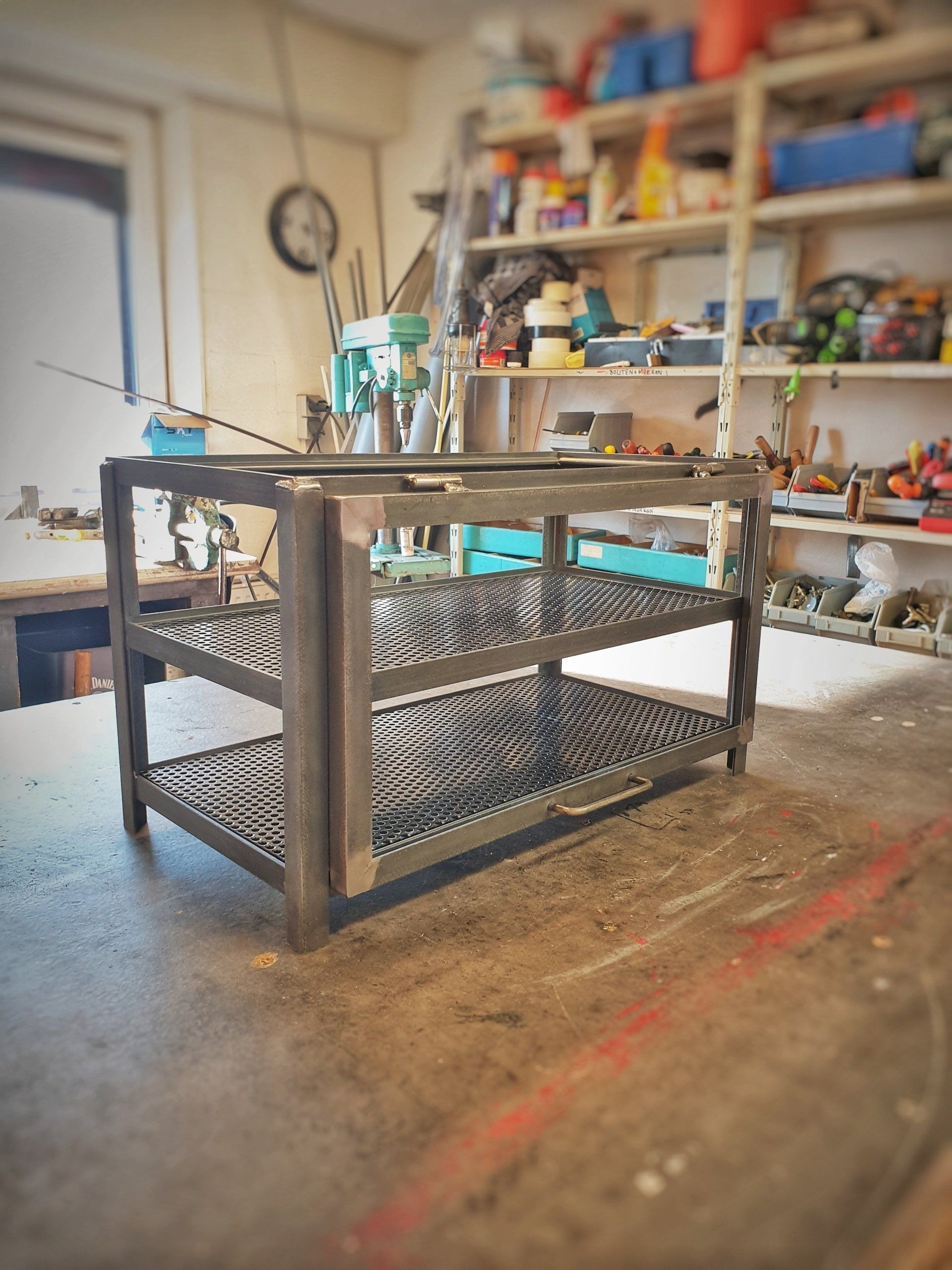 Een metalen stellingkast met twee niveaus en geperforeerde stalen planken, die op de vloer van een werkplaats staat.