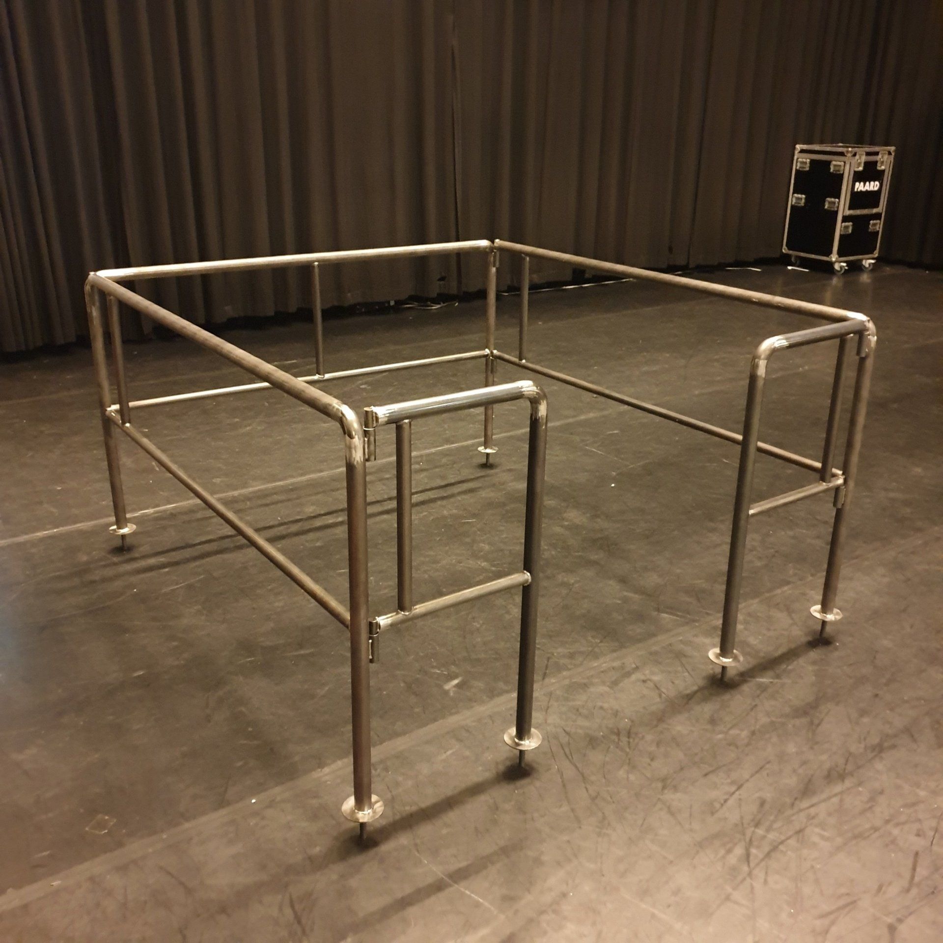 Een metalen buizenconstructie voor de balustrade staat op een donkere vloer in een ruimte met toneelgordijnen.