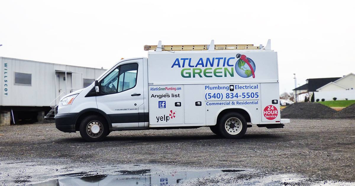 A white Atlantic Green plumbing service utility van parked on a gravel lot.