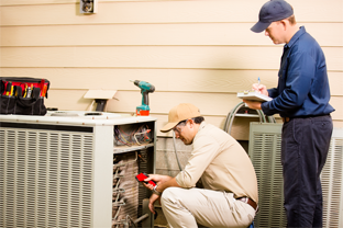 Two technicians inspecting an outdoor HVAC unit, one using a meter, other taking notes.